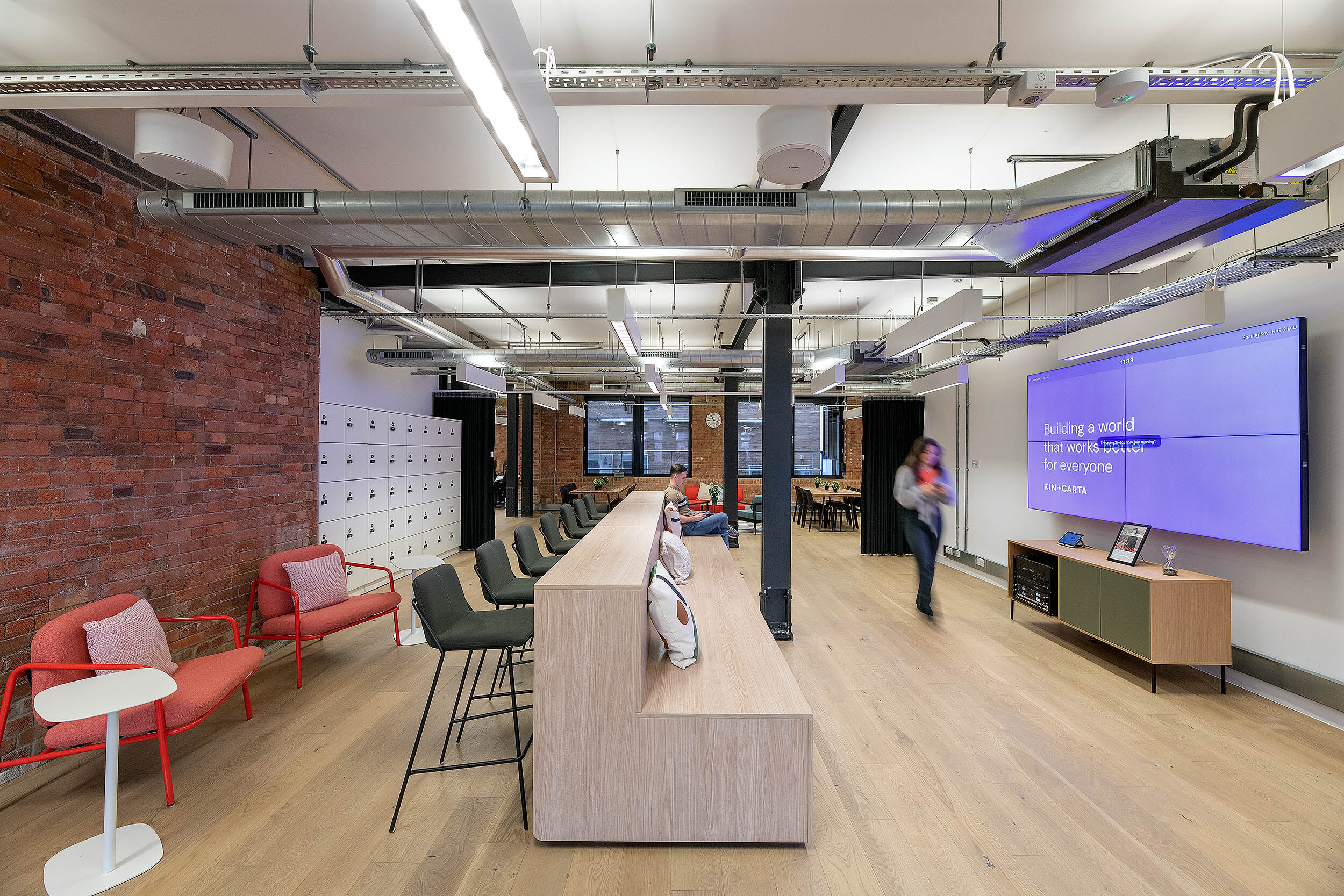 Comfortable seating area at Kin & Carta, designed by Platfform, with red armchairs, a modern bench, and natural wooden flooring in an industrial-style setting.