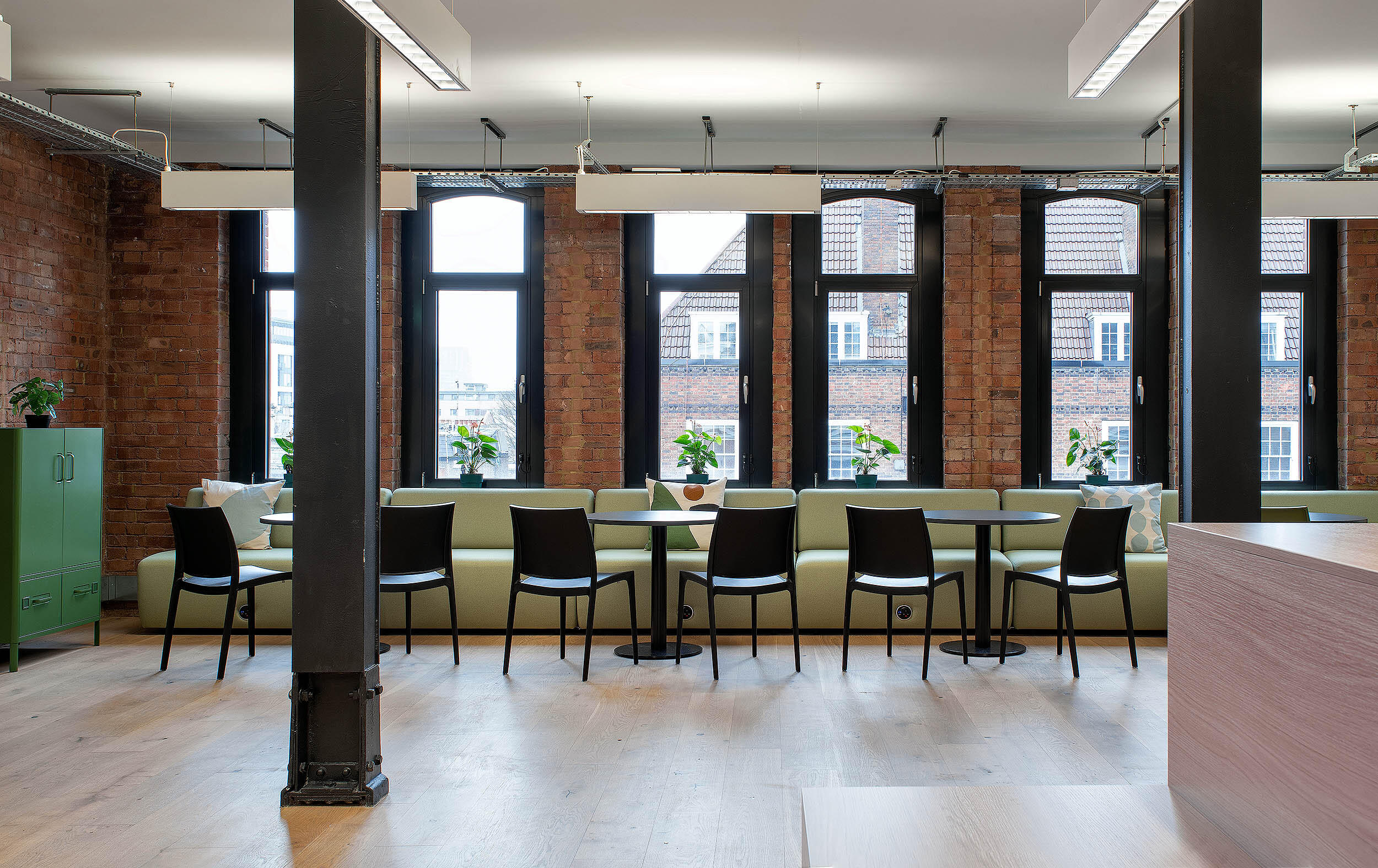 A bright office lounge designed by Platfform, with light green sofas, black chairs, and large windows overlooking the surrounding city.