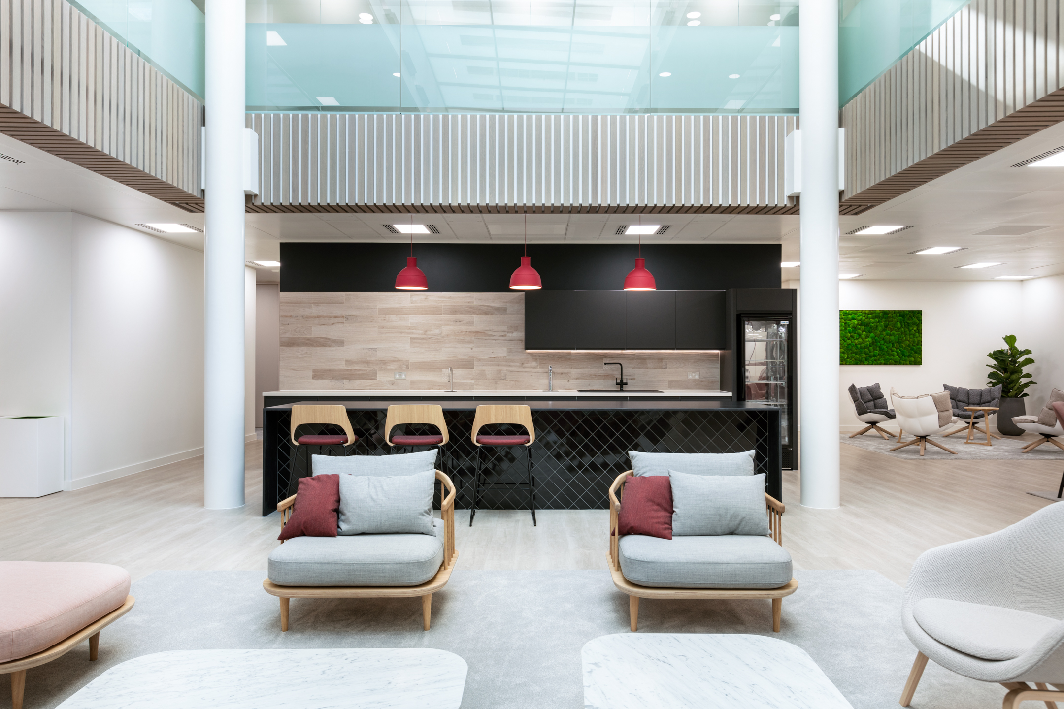 Bright breakout and teapoint area at Marylebone Fujitsu office, showcasing modern lounge chairs, red-accented bar stools, and bold pendant lighting above a black-tiled breakfast bar.