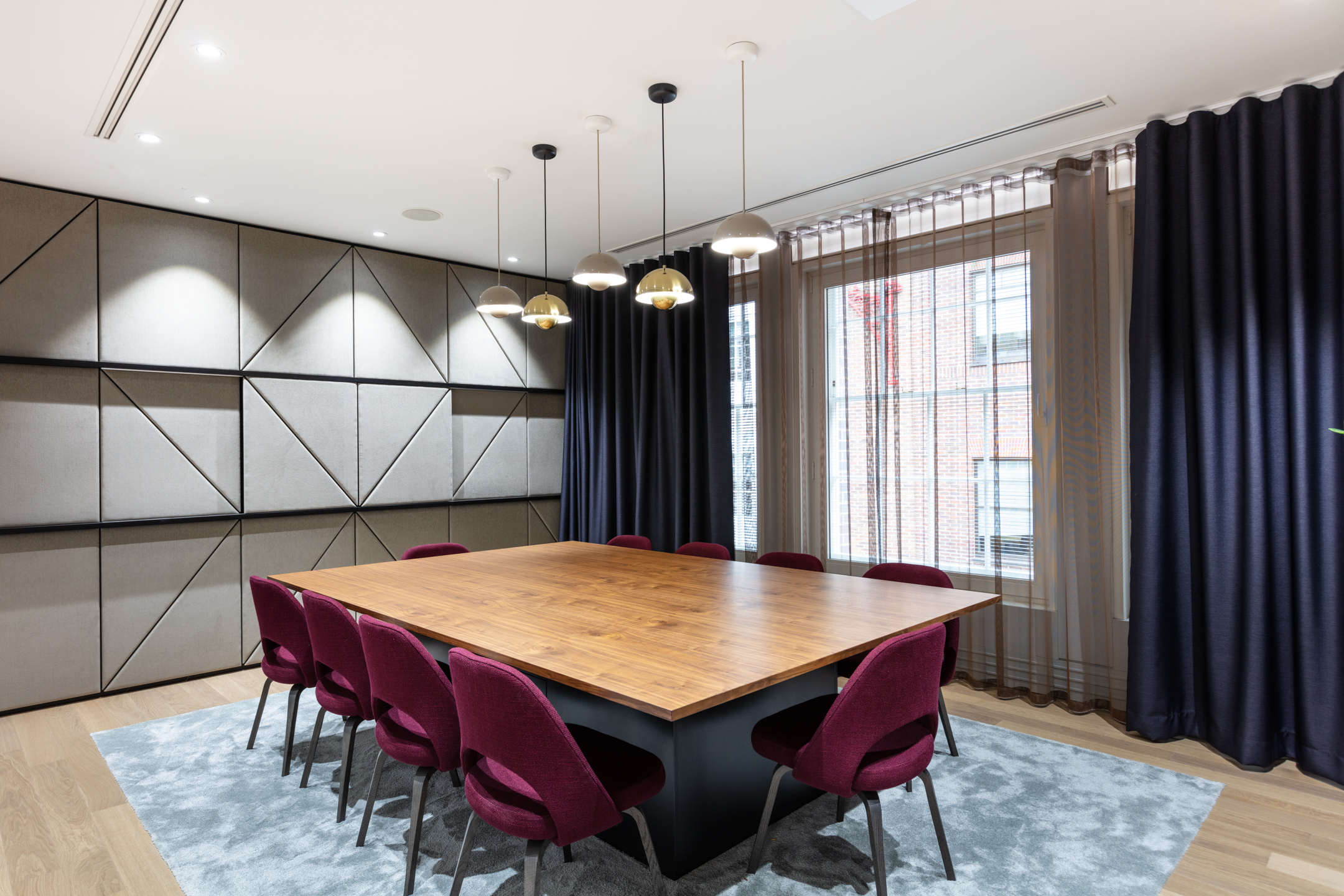 Meeting room at Marylebone Fujitsu office featuring a large wooden table, plum-coloured chairs, acoustic wall panels and layered curtains for a refined, comfortable setting.