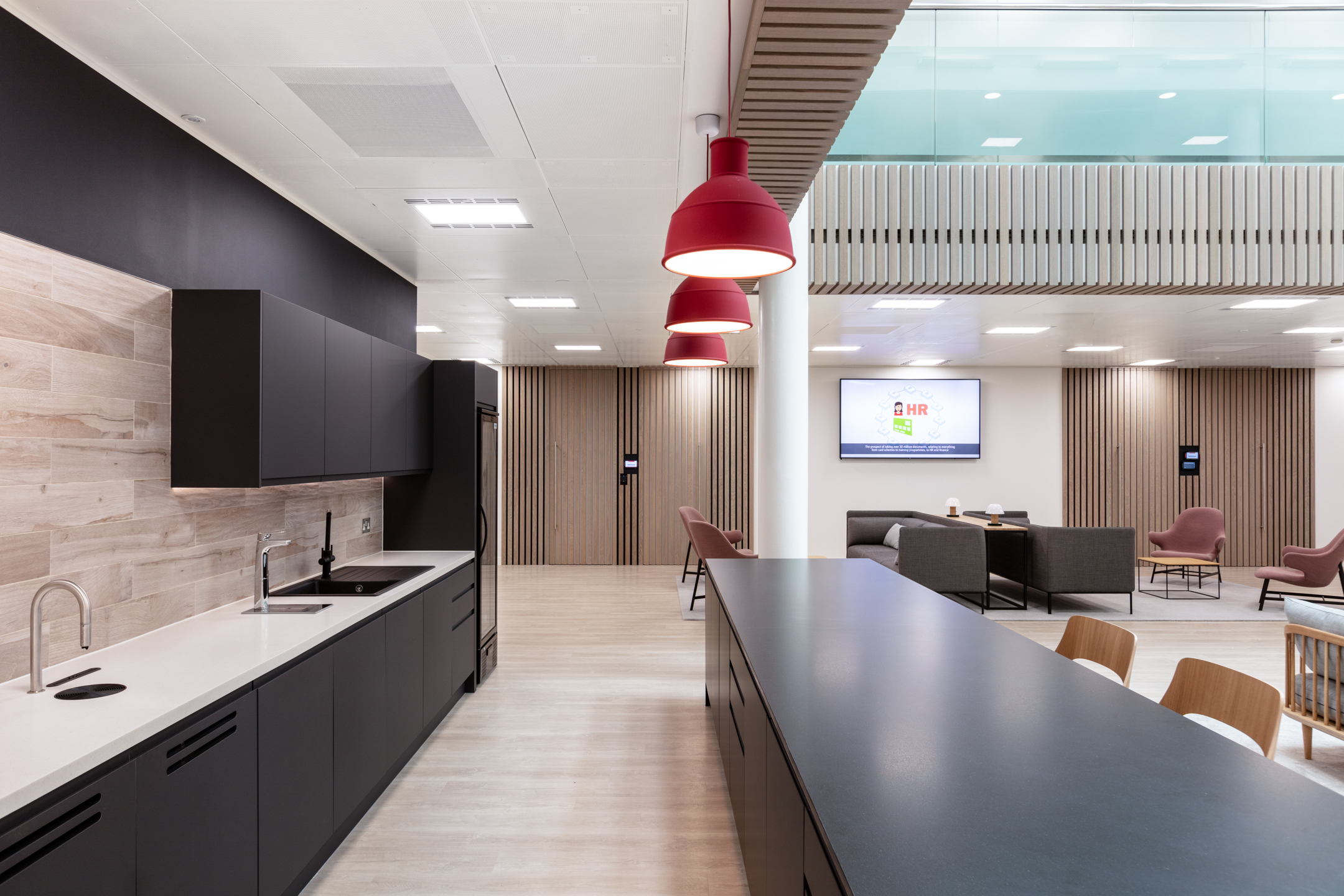 Teapoint area at Marylebone Fujitsu office, with matte black cabinetry, red pendant lights and coordinated furniture across an open-plan setting.