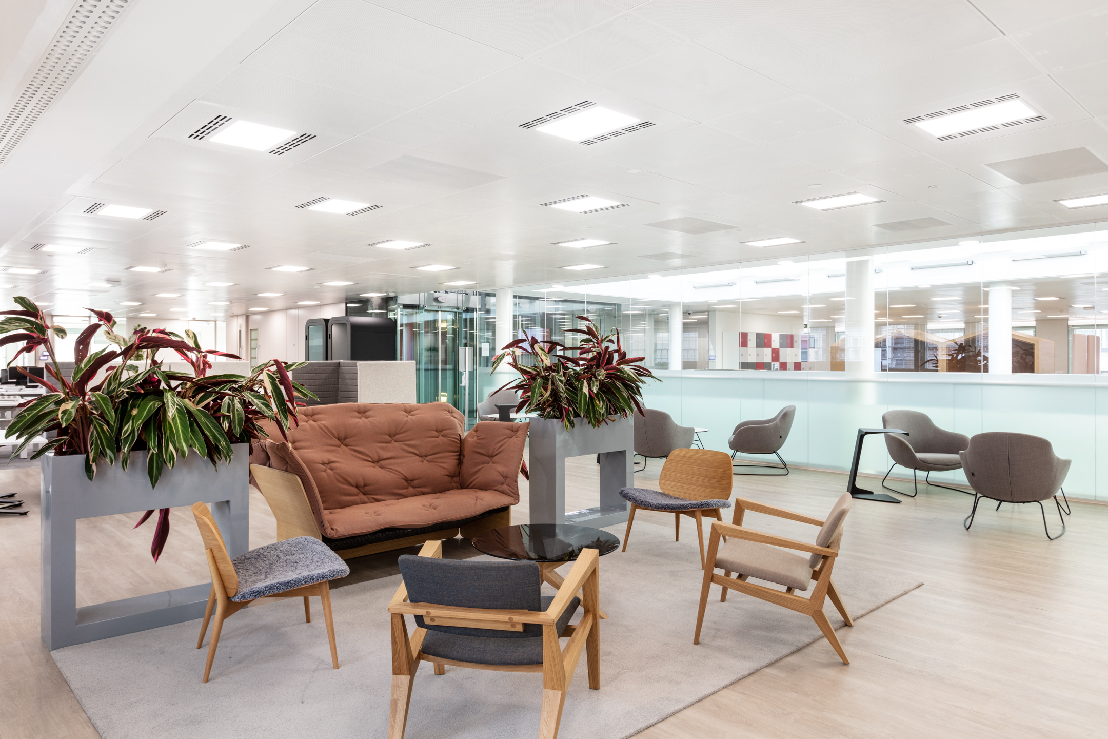 Breakout zone at Marylebone Fujitsu office with mid-century style chairs, a rust-toned sofa and planter dividers bringing greenery into the open-plan workspace.