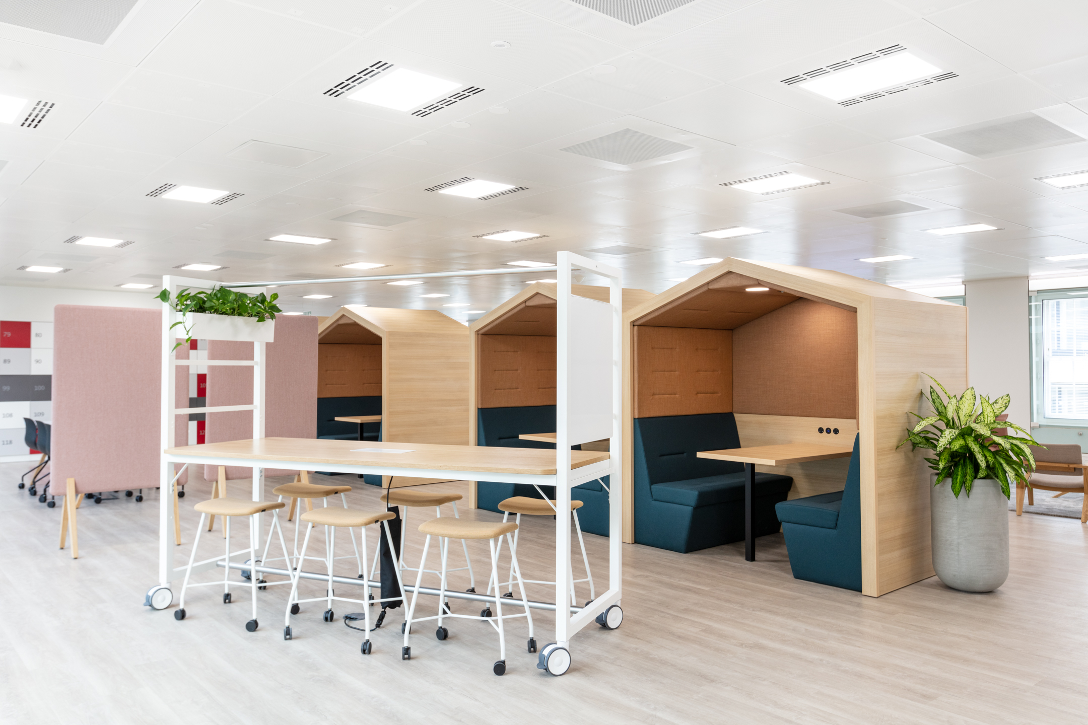 Flexible work zone at Marylebone Fujitsu office with high stools, white mobile tables, and timber-framed meeting pods designed for focused collaboration.