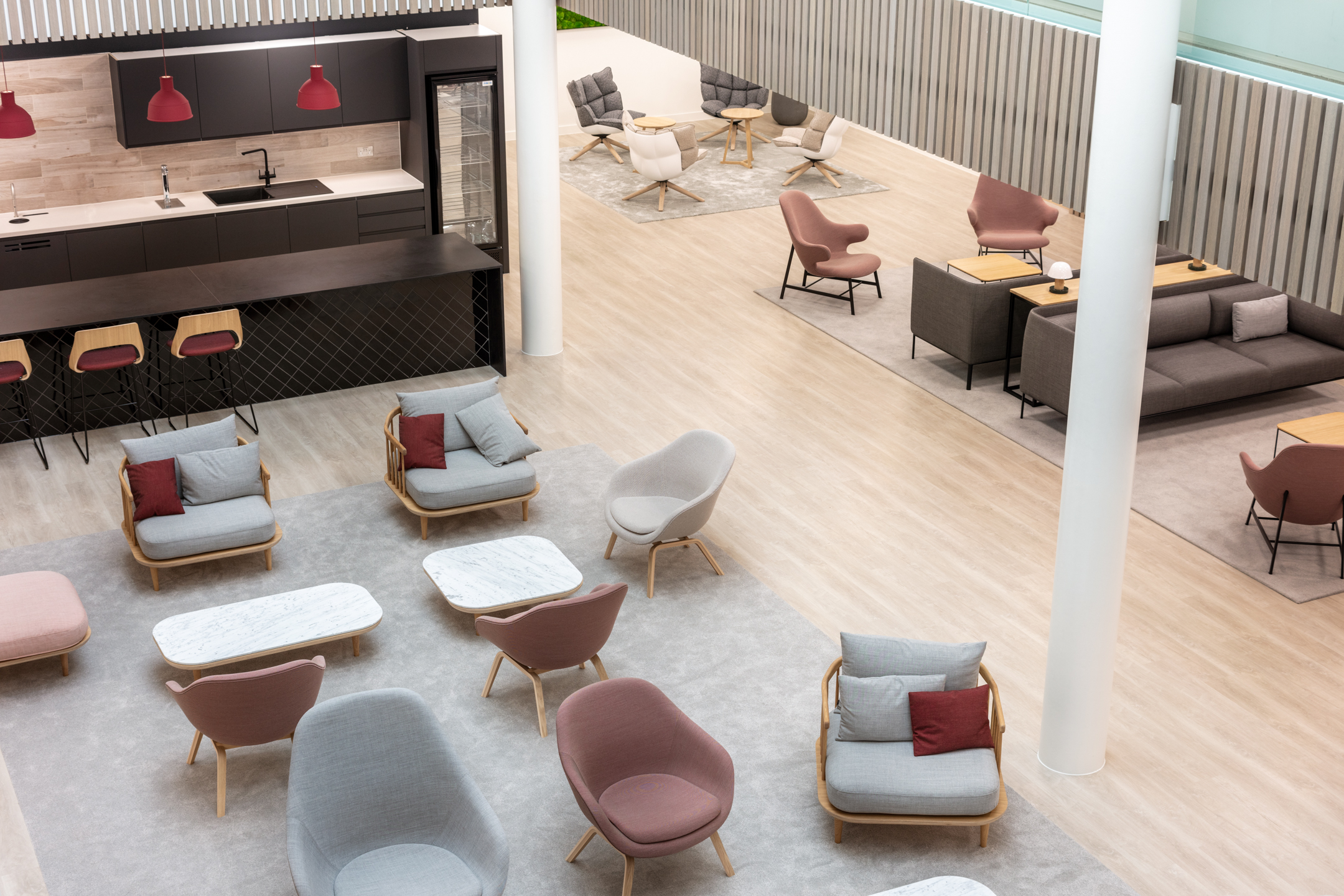Overhead view of the Marylebone Fujitsu breakout area, highlighting a variety of soft seating, marble tables and a sleek kitchen area with red accents.