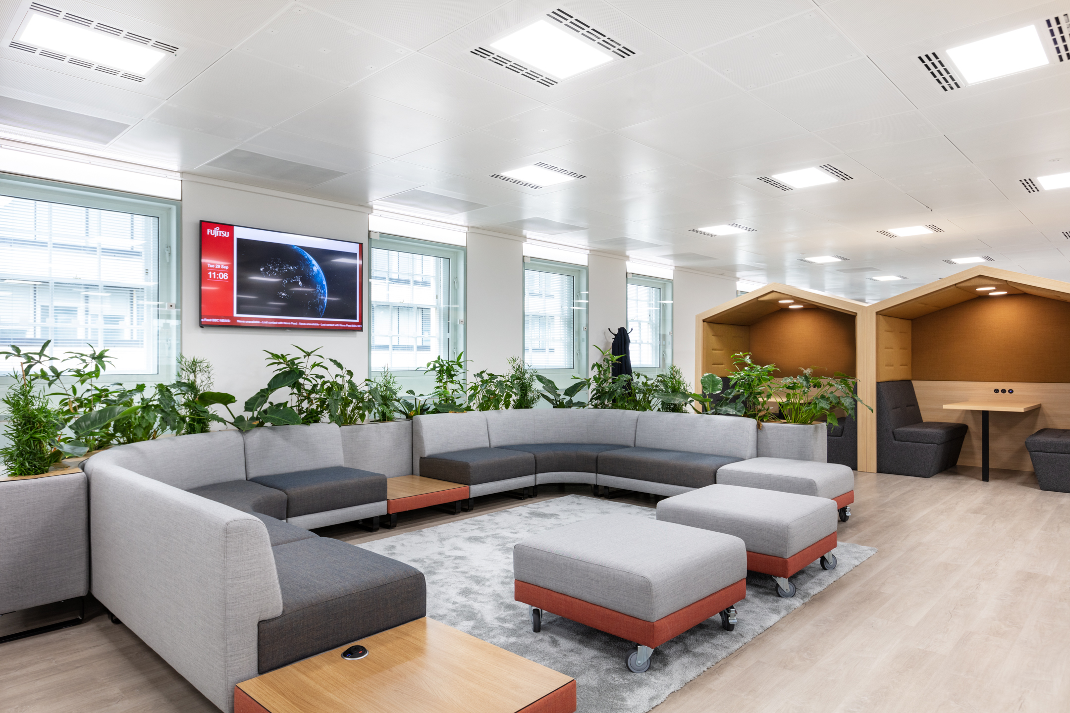 Collaborative breakout area at Marylebone Fujitsu office with modular seating, soft grey upholstery, built-in planters and timber-framed booths for informal meetings.