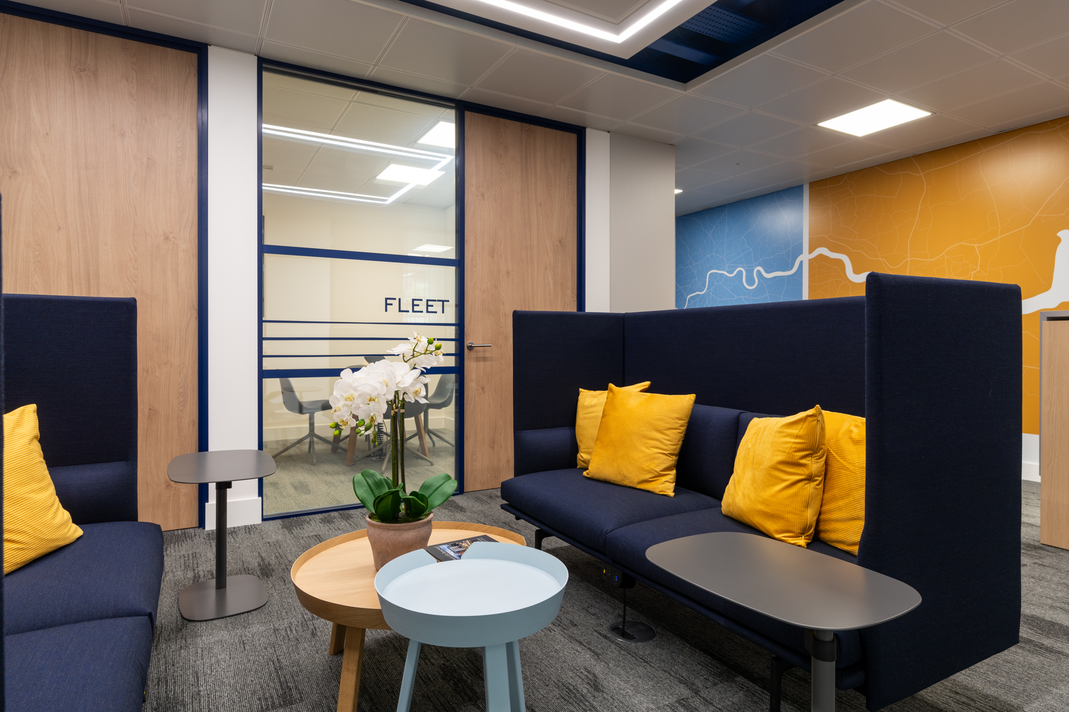 Informal seating area at the Port of London Authority office by Platfform, featuring navy high-back sofas, yellow cushions, and a river-themed mural.