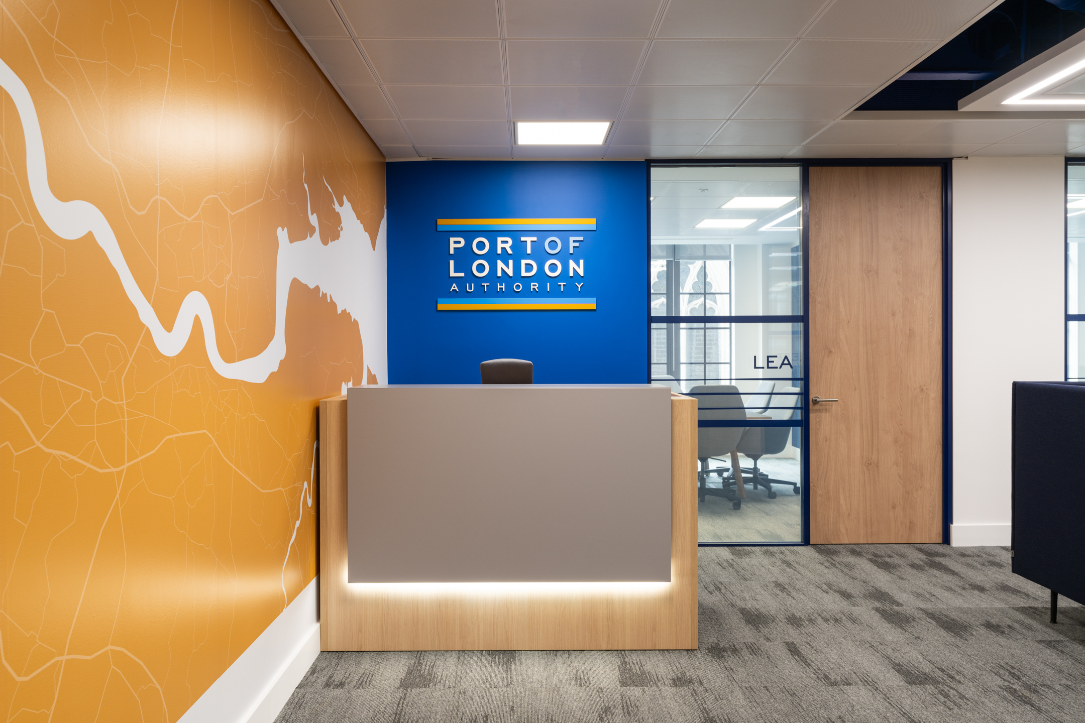 Reception area at the Port of London Authority office by Platfform, featuring a branded wall with river graphics, a sleek desk, and glass meeting room doors.