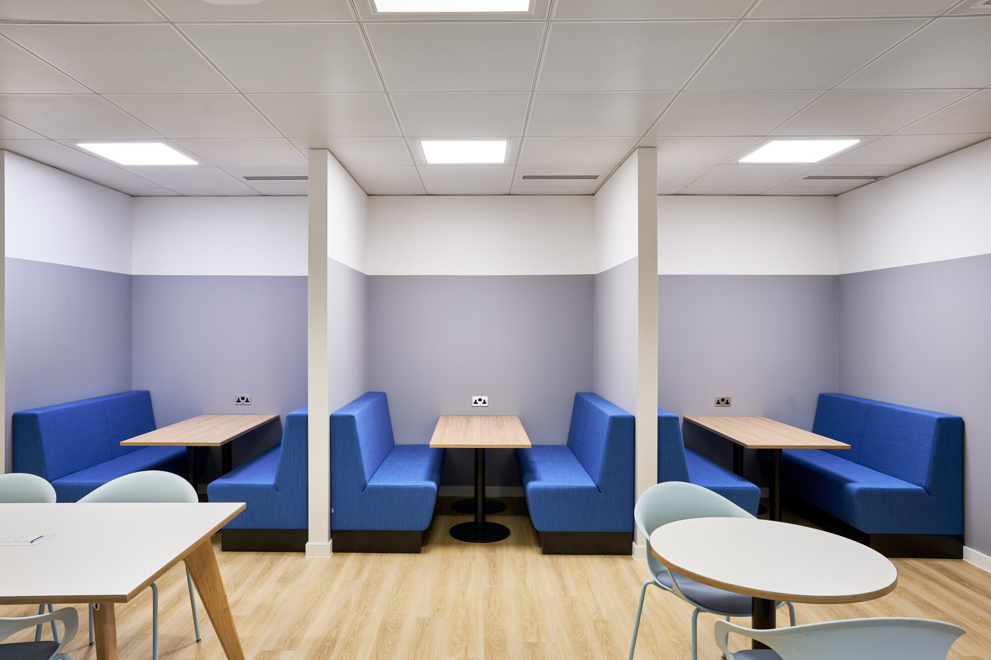 Tech UK office featuring a lively common area with blue sofas and private booth seating for focused work.