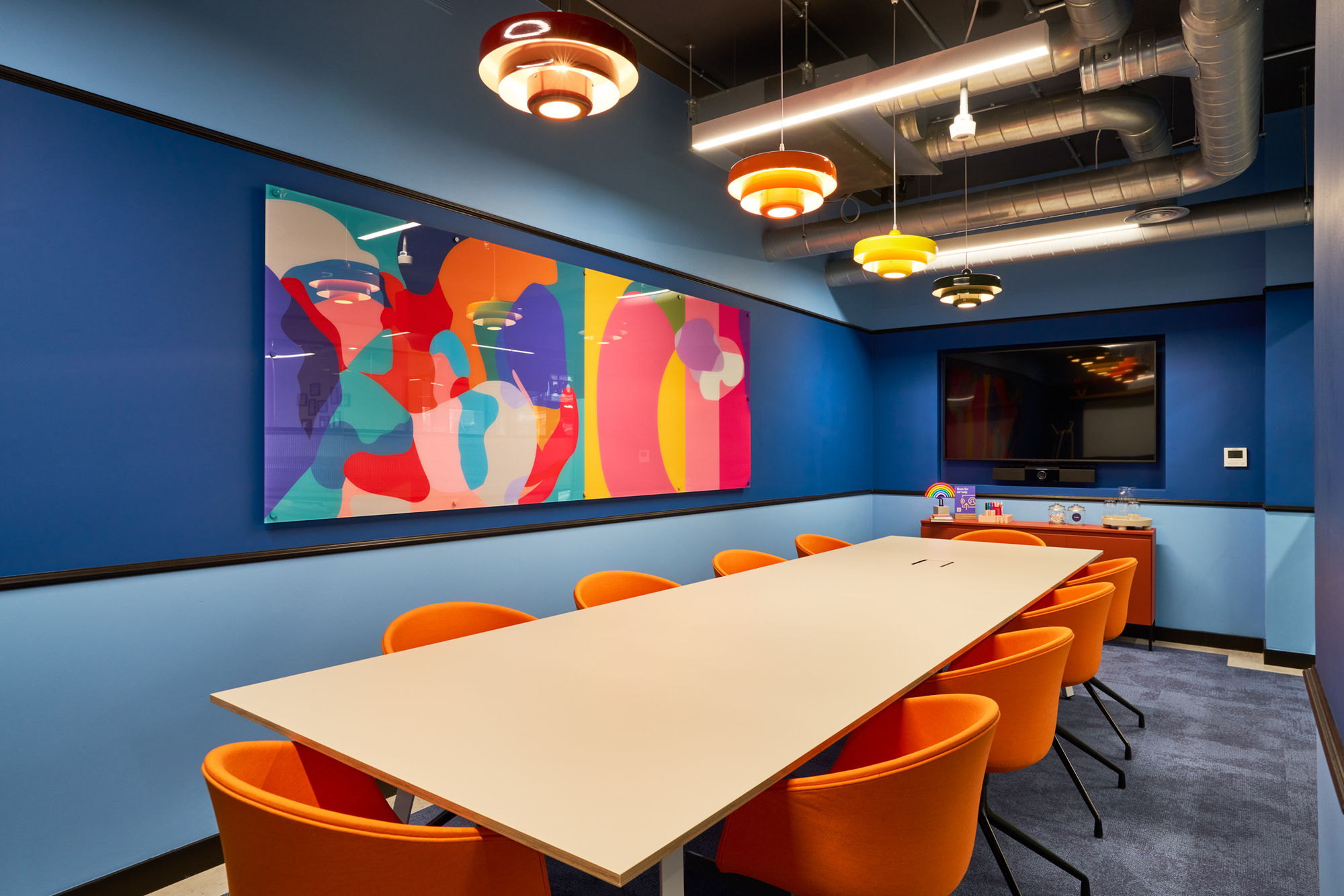 The vibrant meeting room “Pride” at Work.Life Waverly House by Platfform, featuring bold blue walls, orange chairs, and colourful artwork inspired by Soho's energy.