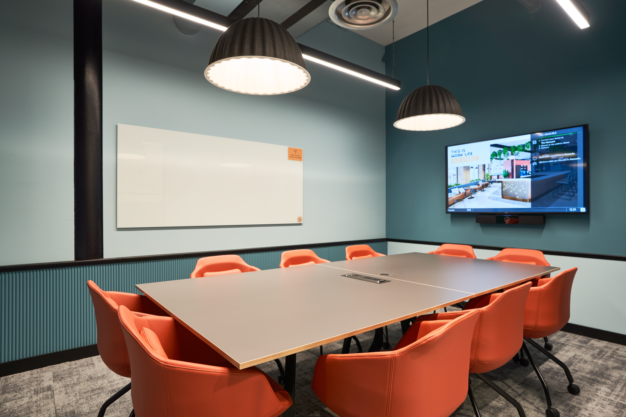 A vibrant meeting room at Work.life Rivington House by Platfform, featuring a large table, bright orange chairs, and contemporary lighting in a flexible workspace.