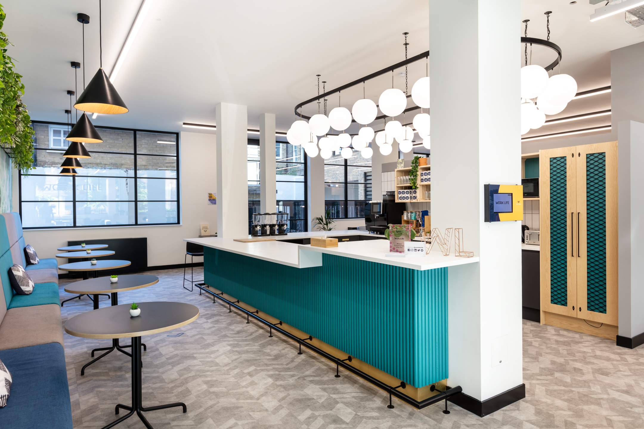 A vibrant communal workspace at Work.life Red Lion Street featuring a sleek turquoise bar counter, stylish pendant lighting, and cosy seating, designed to inspire productivity and collaboration by Platfform.