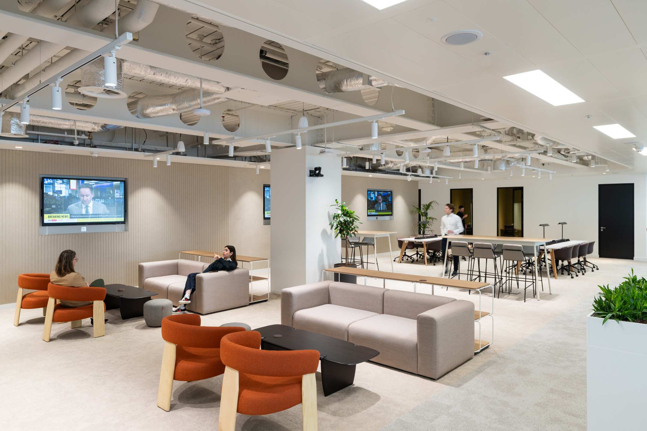 Ark Syndicate breakout space with soft seating, bold orange chairs, and high tables designed for both focus and downtime.
