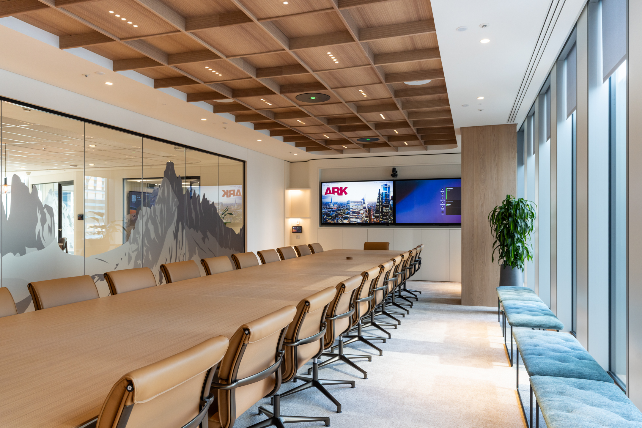 Ark Syndicate boardroom with tan leather chairs, wood-panel ceiling and double screens styled for confident conversations and big decisions.
