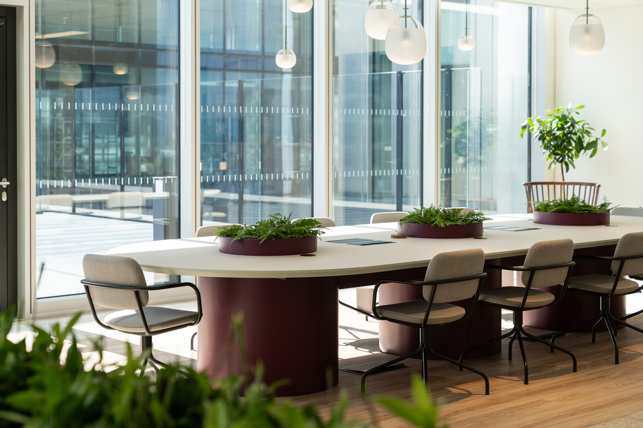 Ark Syndicate collaboration table with soft chairs and built-in planters surrounded by natural light and leafy views of the terrace.