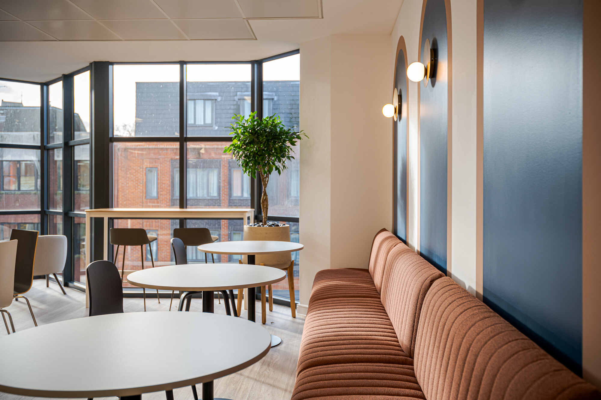 Layered seating at Accelya’s teapoint with ribbed upholstery and arched blue panelling, styled by Platfform to echo retro cabin lounge design.