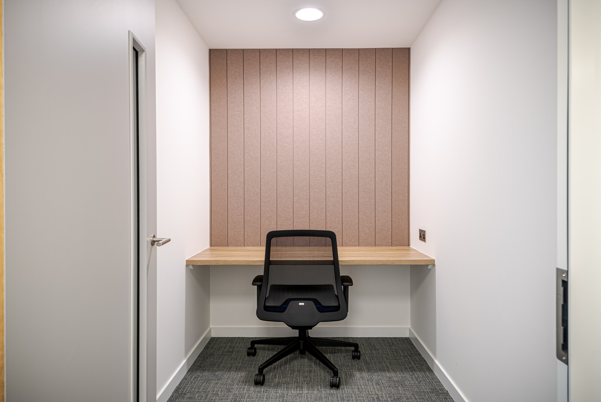 Compact focus room at Accelya with a timber desk, upholstered acoustic panelling and mesh task chair, furnished by Platfform for quiet concentration.