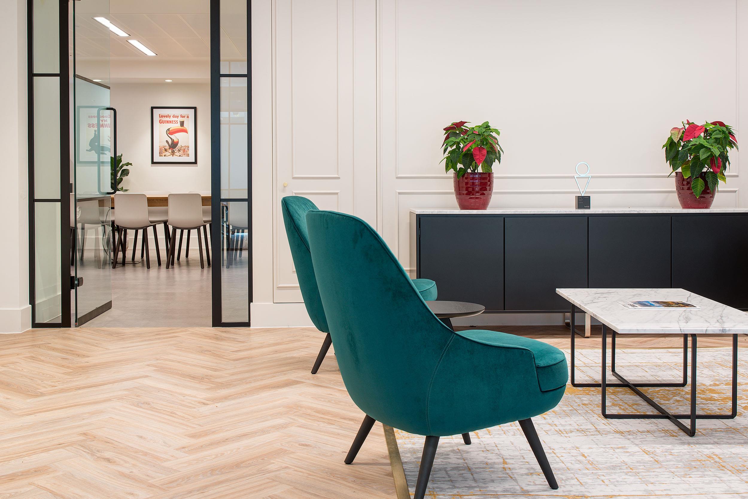 Detail of the lounge area at Guinness Asset Management with Platfform-supplied teal armchairs, a marble coffee table, and a view into the meeting room.
