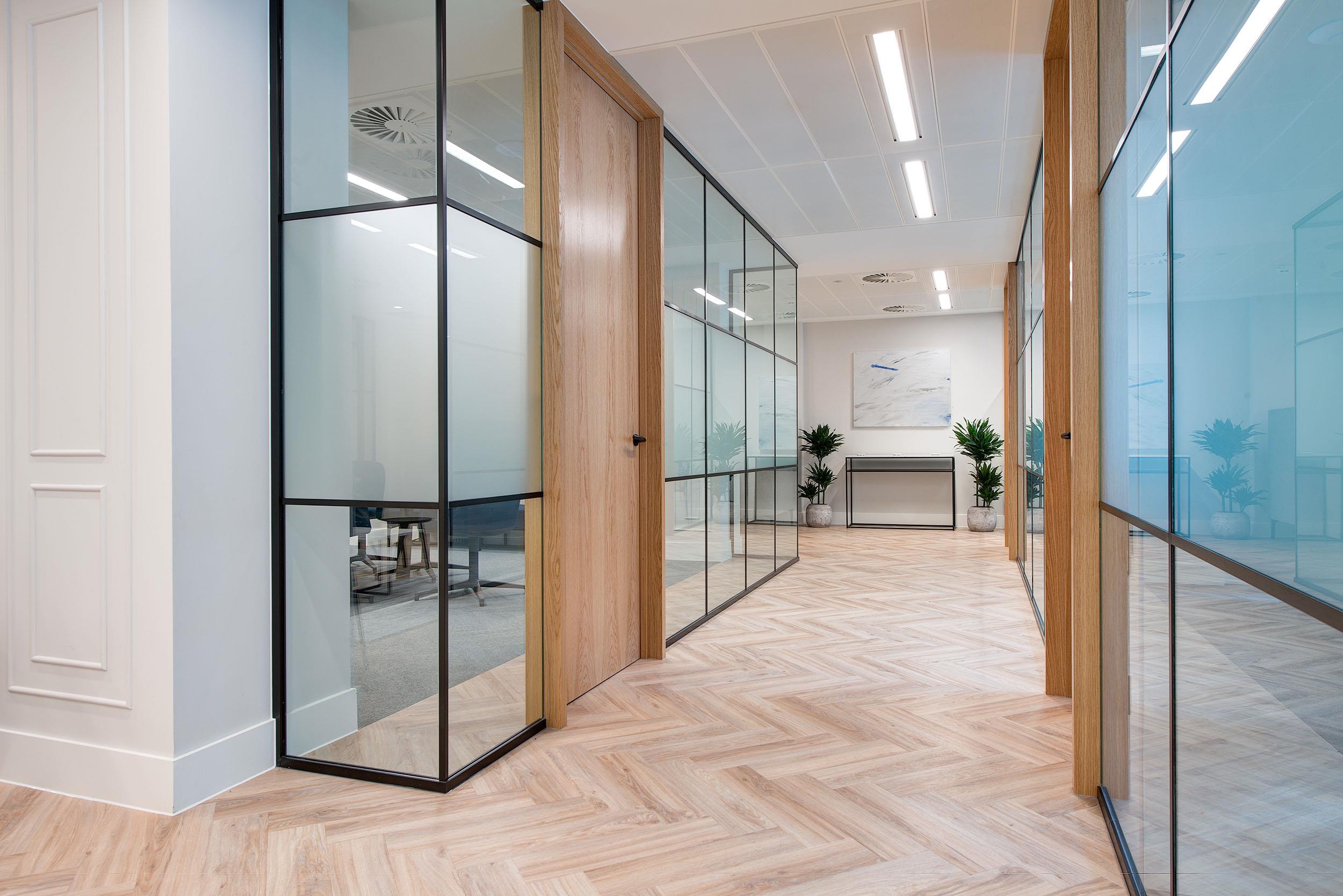 Glazed corridor with oak-framed meeting rooms at Guinness Asset Management, with Platfform furniture visible through the frosted glazing partitions.