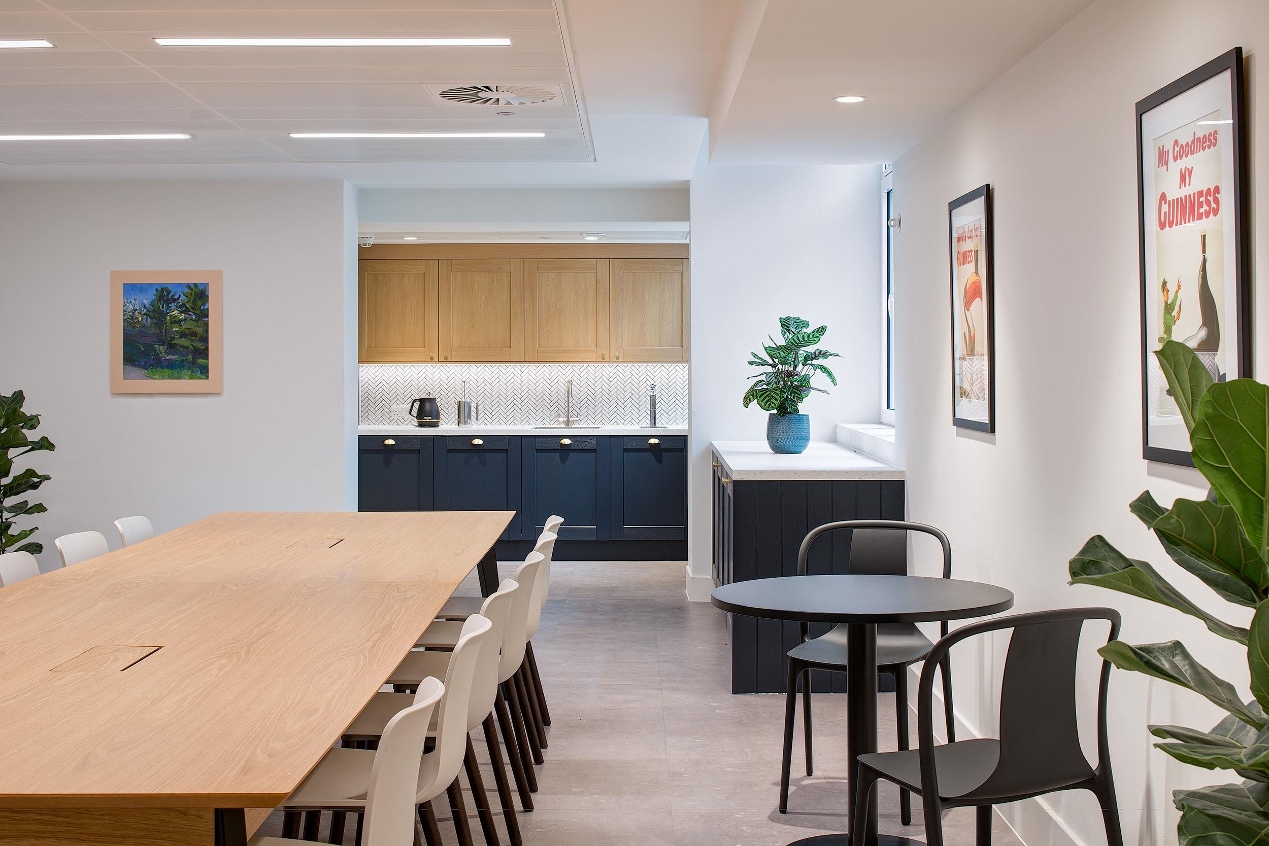 Teapoint and breakout area at Guinness Asset Management, furnished by Platfform with a long communal table, black café seating, and integrated kitchen cabinetry.