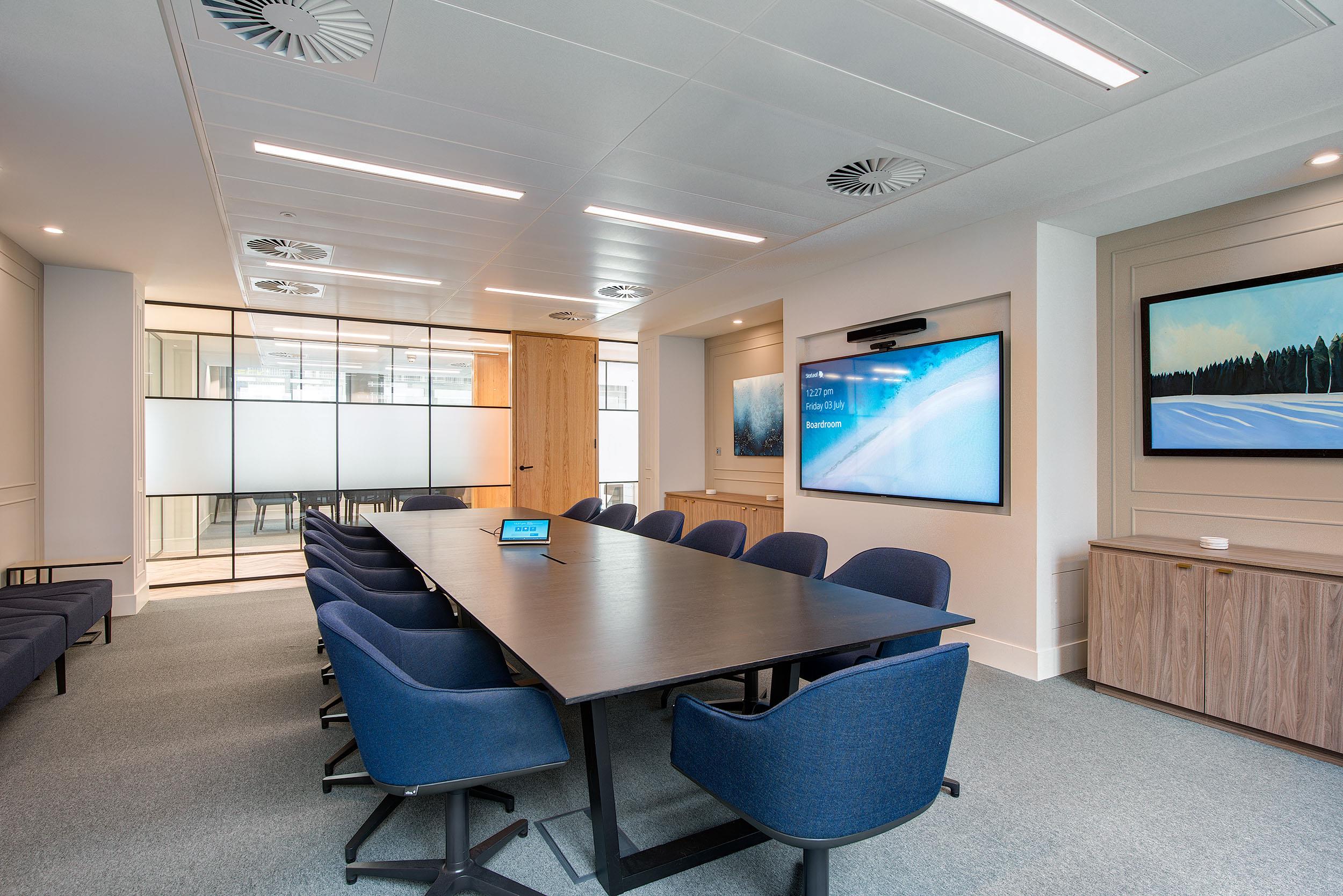 Meeting room at Guinness Asset Management with Platfform-supplied navy upholstered chairs, black conference table, and integrated AV screens.
