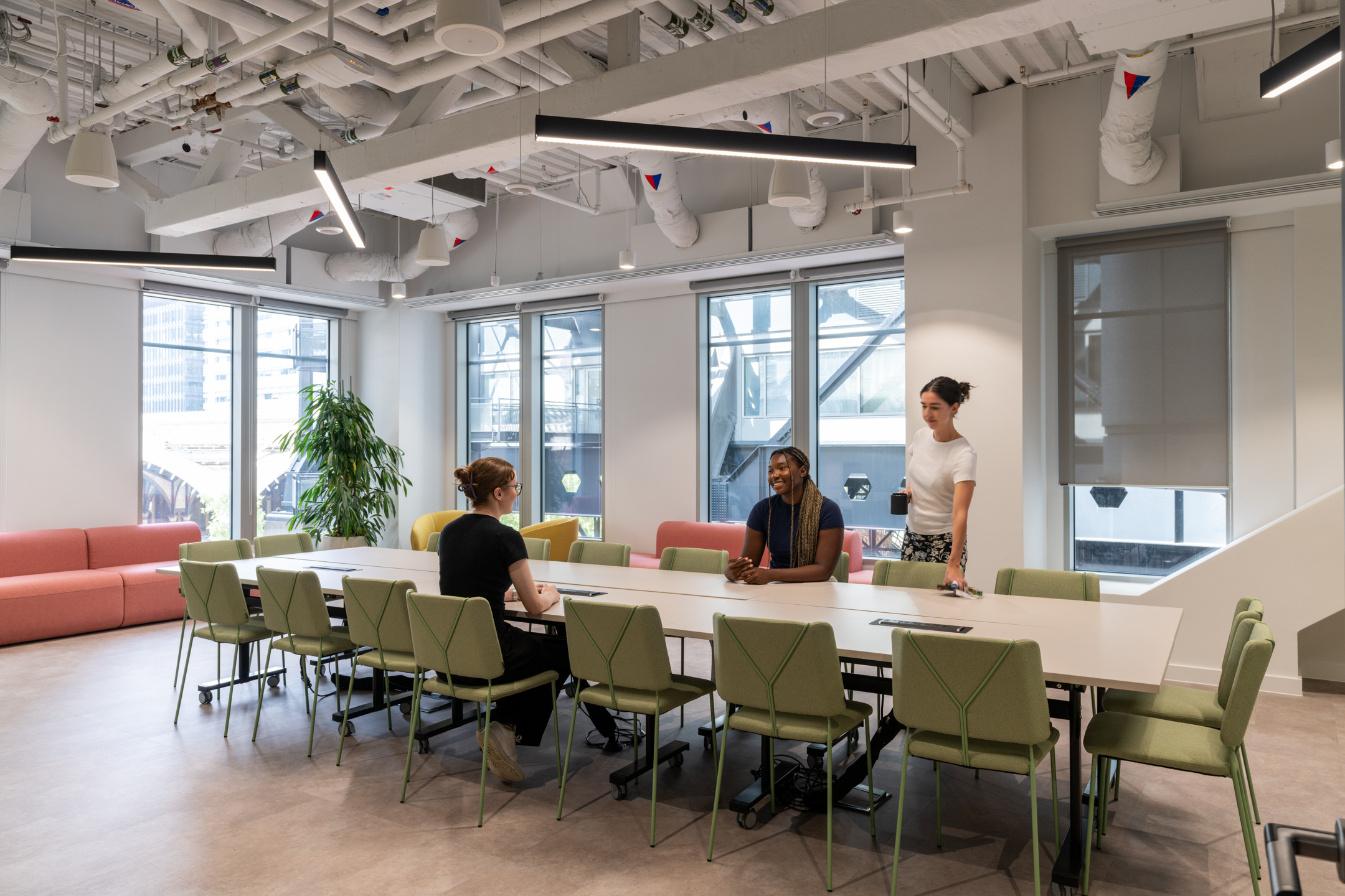 Meeting space at Huckletree, Bishopsgate, with a long white table, green upholstered chairs and pastel sofas set against floor-to-ceiling windows.