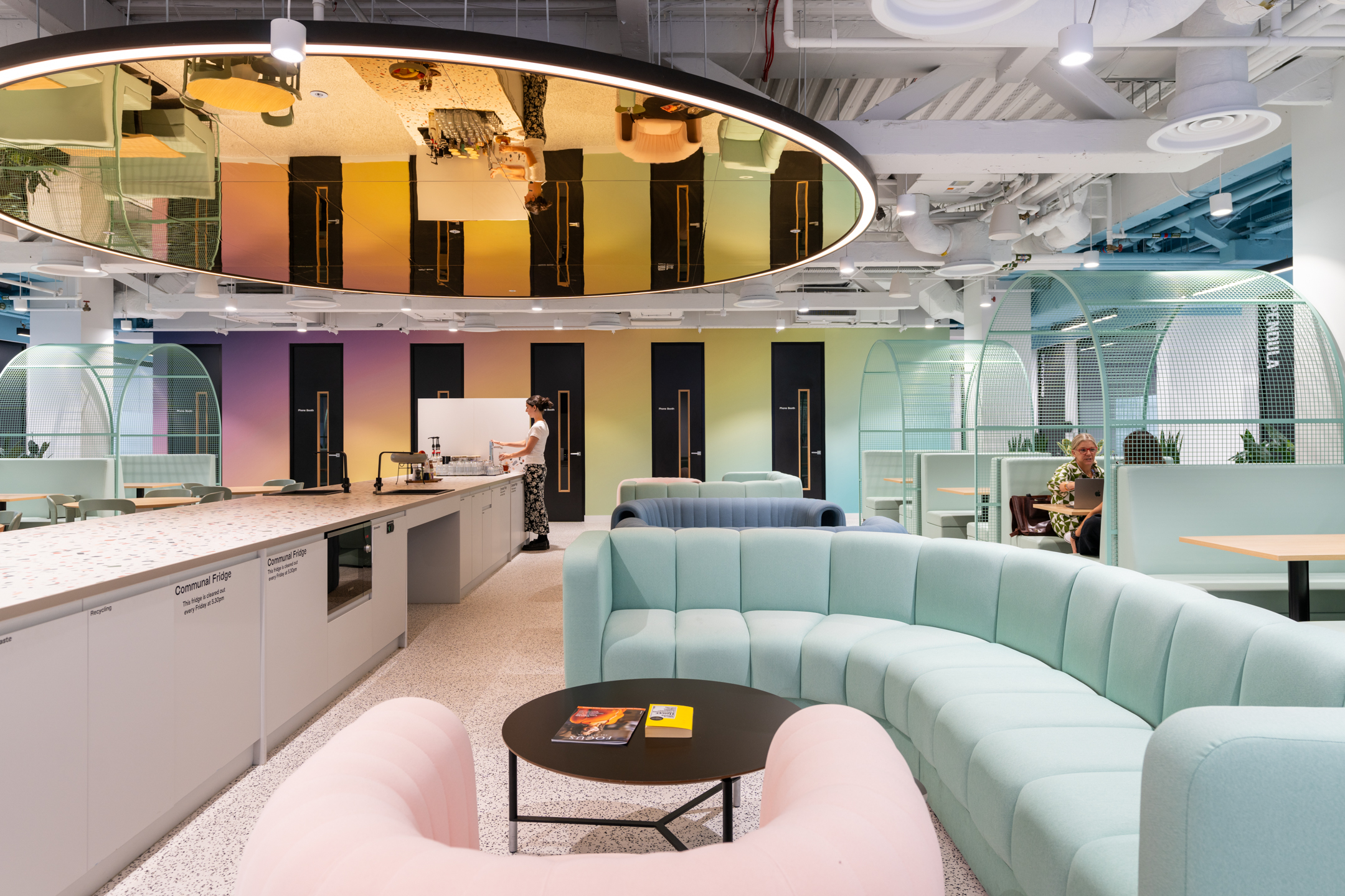Soft seating and teapoint area at Huckletree, Bishopsgate, with curved pastel sofas, terrazzo worktops and mint green booth seating beneath a mirrored ceiling feature.
