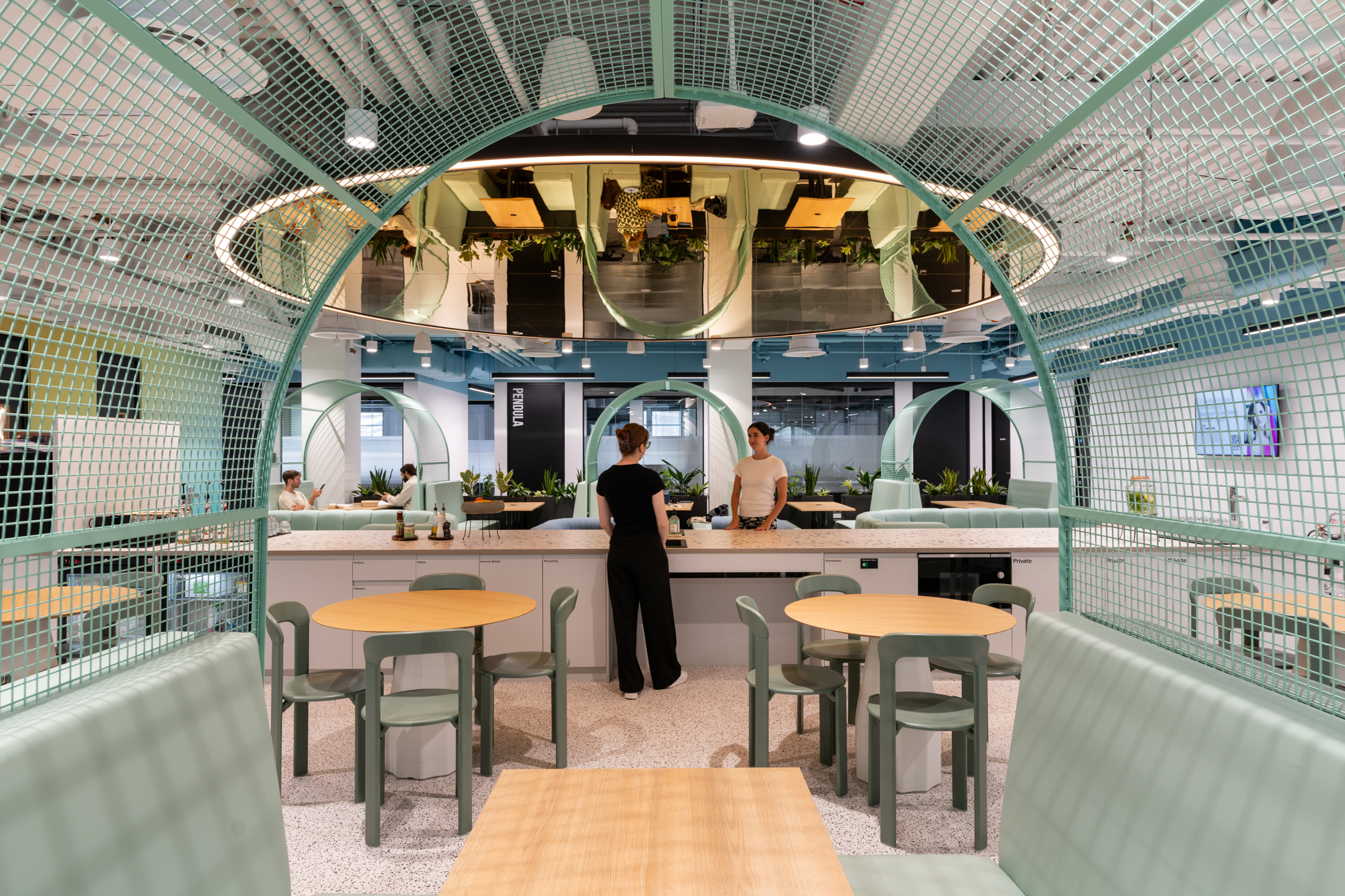 Booth seating and communal teapoint at Huckletree, Bishopsgate, framed by mint green mesh arches and a mirrored ceiling above terrazzo counters and round tables.