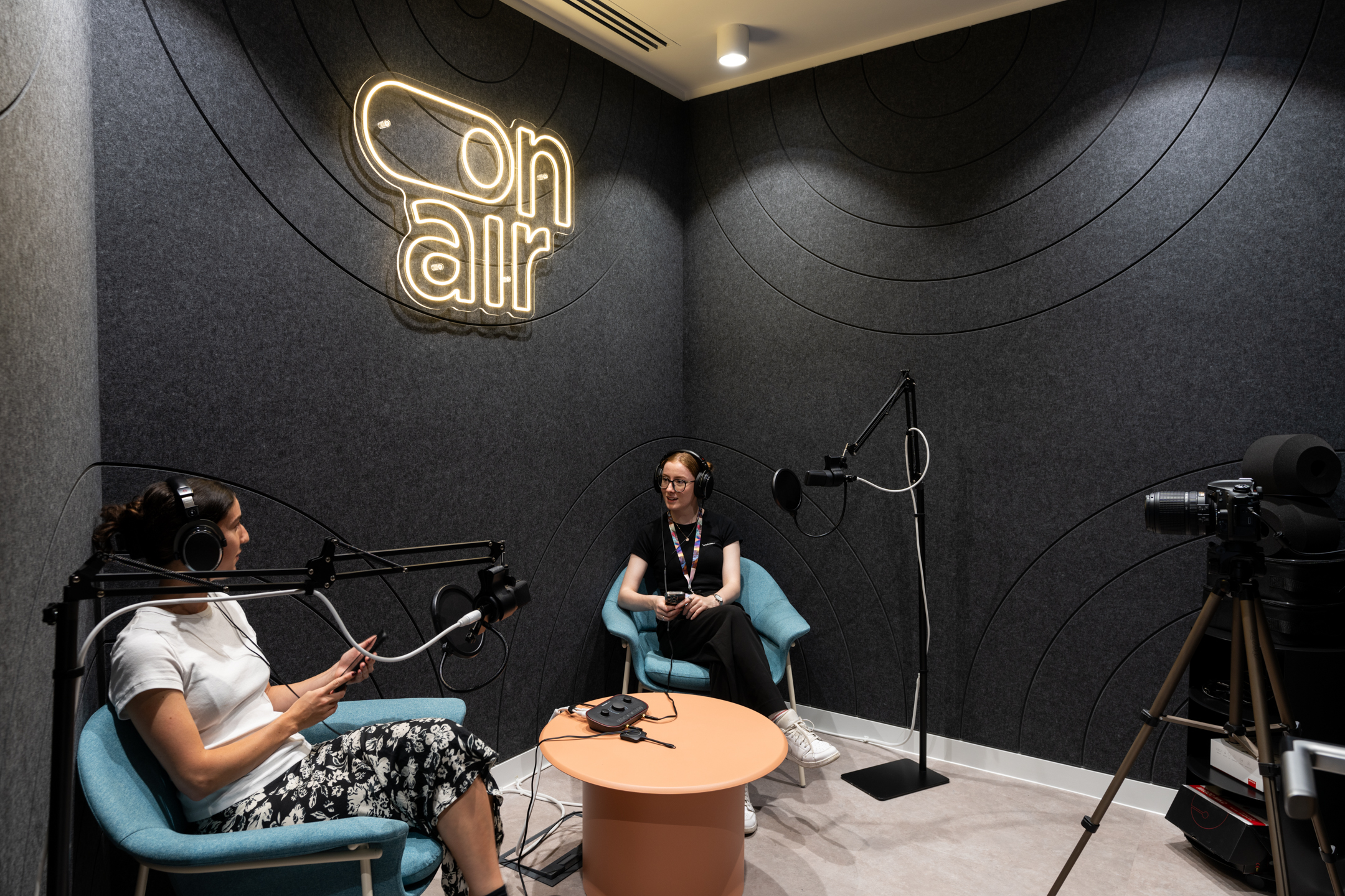 Podcast studio at Huckletree, Bishopsgate, with acoustic panelled walls, mid-century style lounge chairs and recording equipment beneath a glowing 'on air' sign.