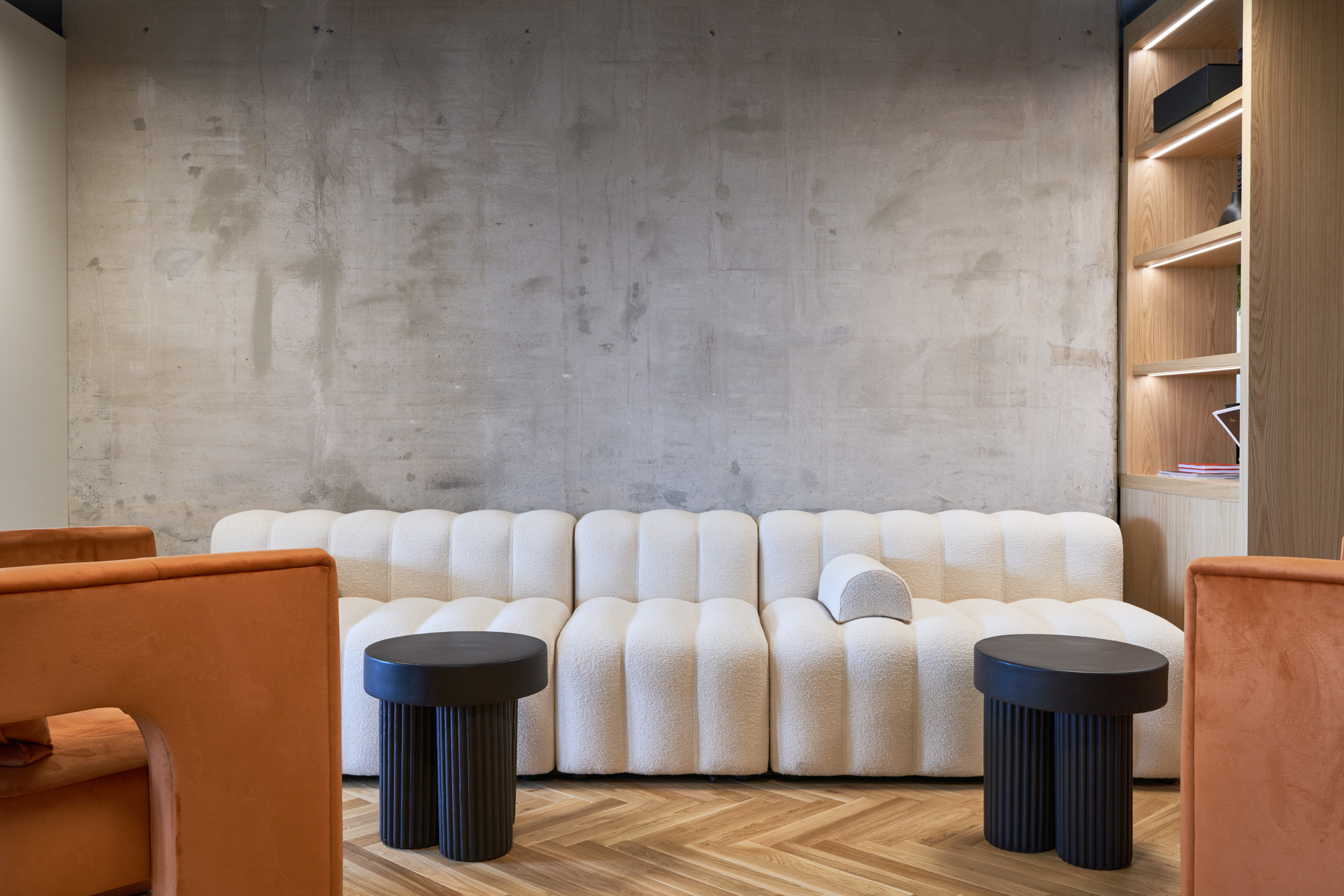 Minimalist lounge at HYLO with a sculpted boucle sofa, rust velvet armchairs and fluted black tables, furnished by Platfform.
