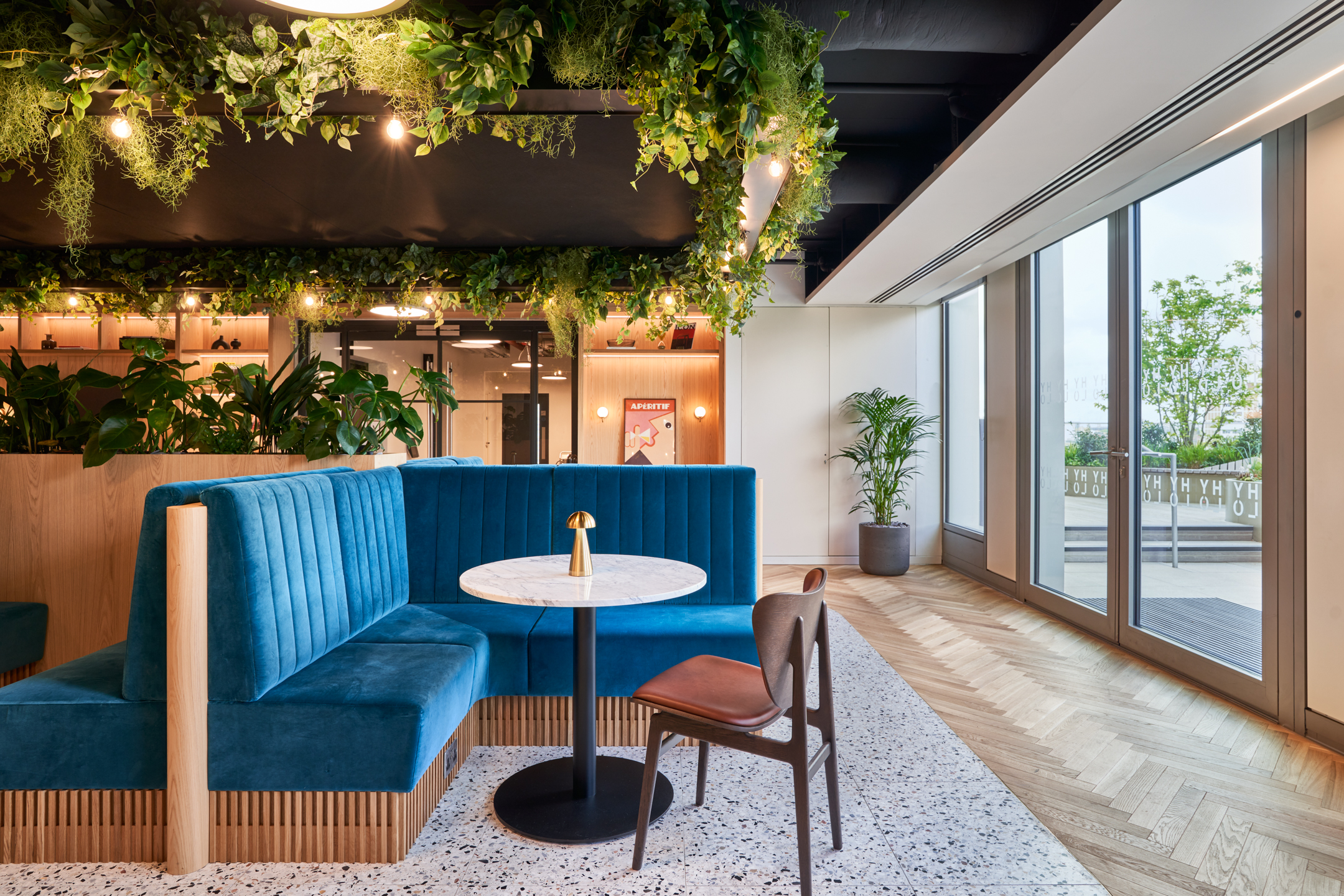 HYLO breakout space with curved teal booth seating, marble café tables and rich greenery, with all furniture specified and supplied by Platfform.