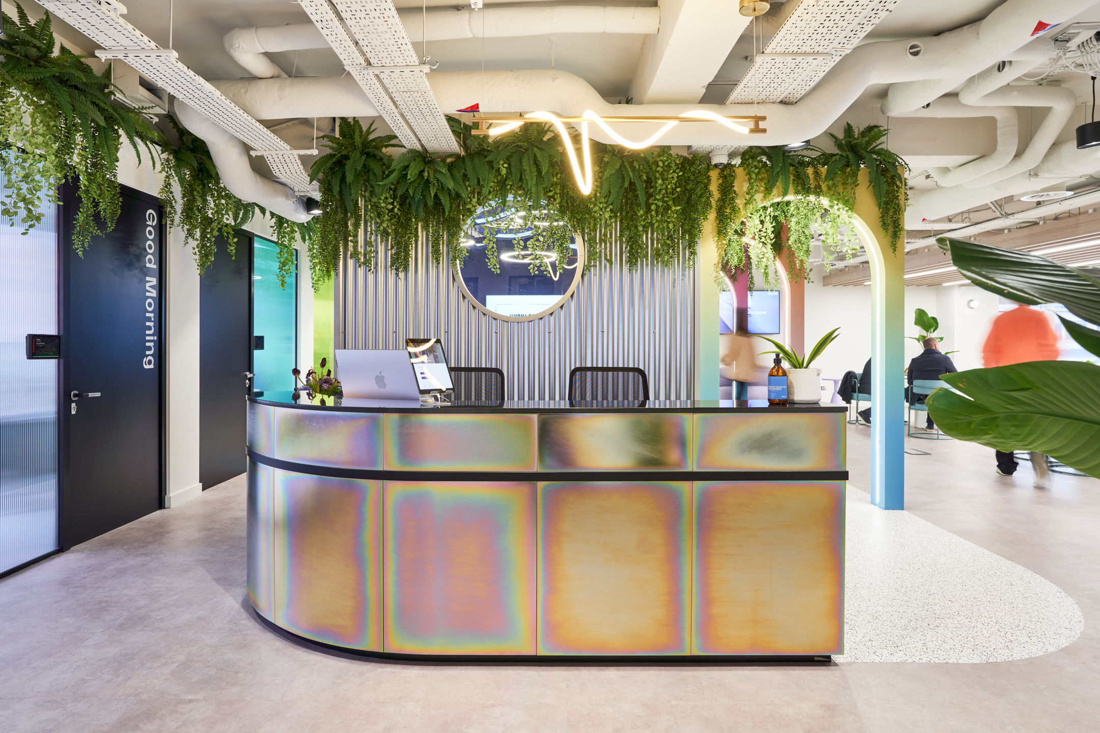 Reception area at Huckletree Oxford Street featuring a rainbow-iridescent desk, hanging greenery and vibrant furnishings supplied by Platfform.
