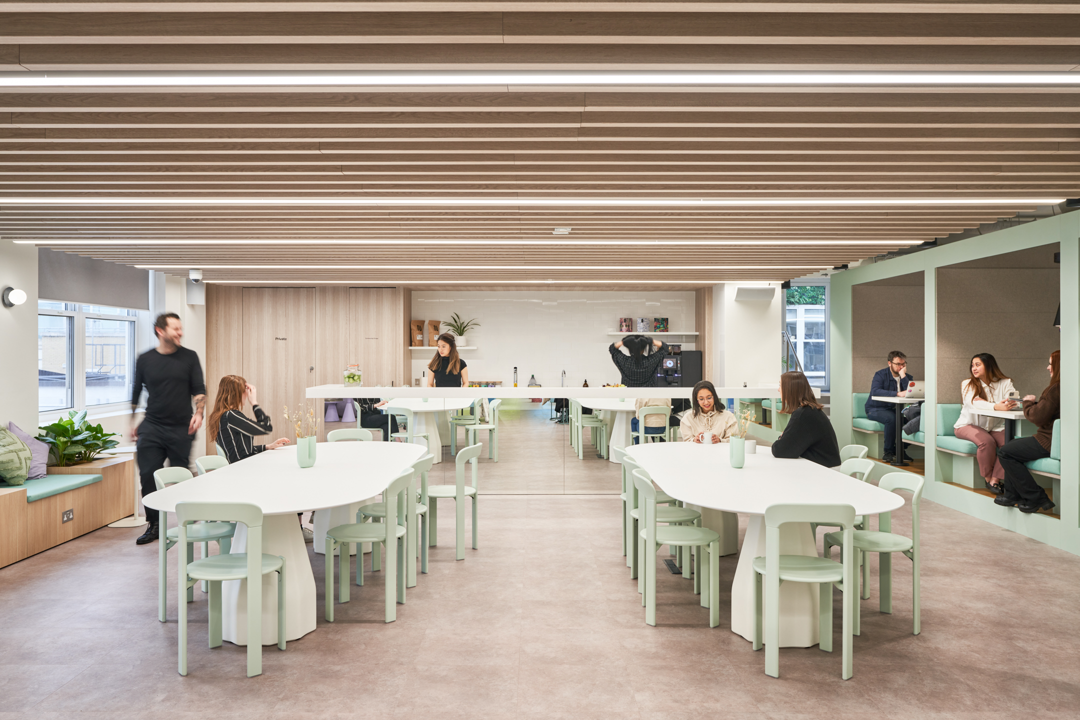 Open-plan communal space at Huckletree Oxford Street, with pale green chairs, curved white tables and banquette booths, all furnished by Platfform.
