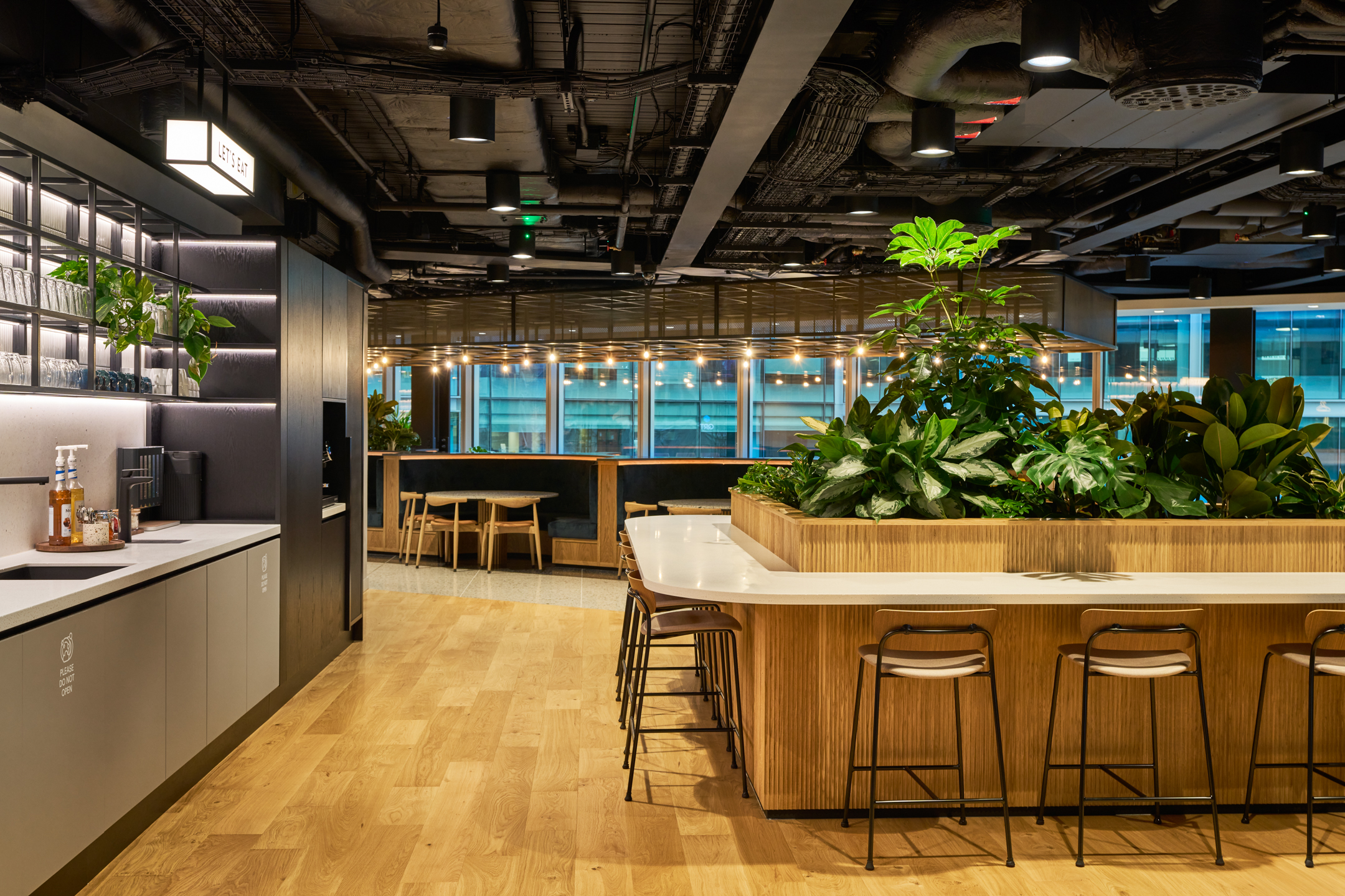 Central refreshment zone at International Technology and Data Firm with layered planting, timber finishes, and built-in seating for informal meetups.