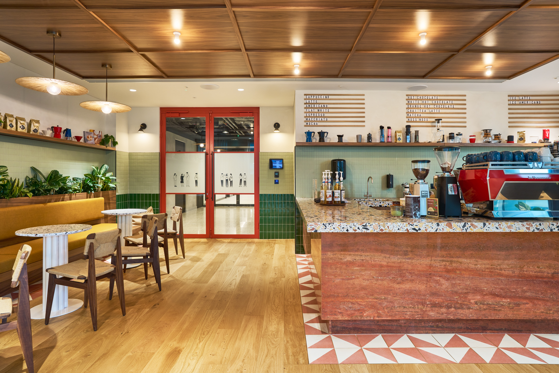 Charity-run barista bar at International Technology and Data Firm featuring terrazzo surfaces, warm timber tones, and custom seating for casual coffee breaks.