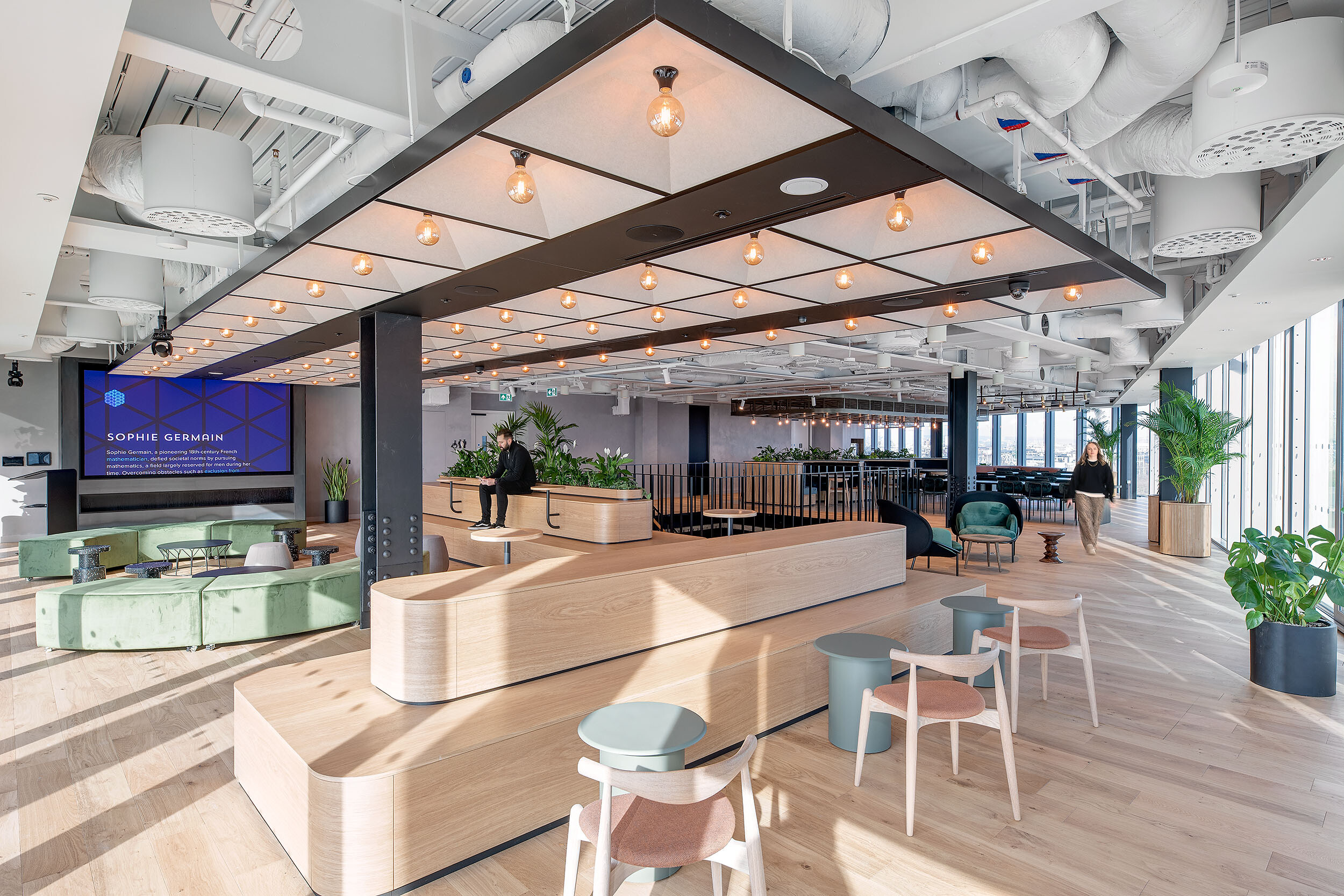 Multifunctional breakout space at International Technology and Data Firm with layered timber seating, green lounge zones and views across the city skyline.