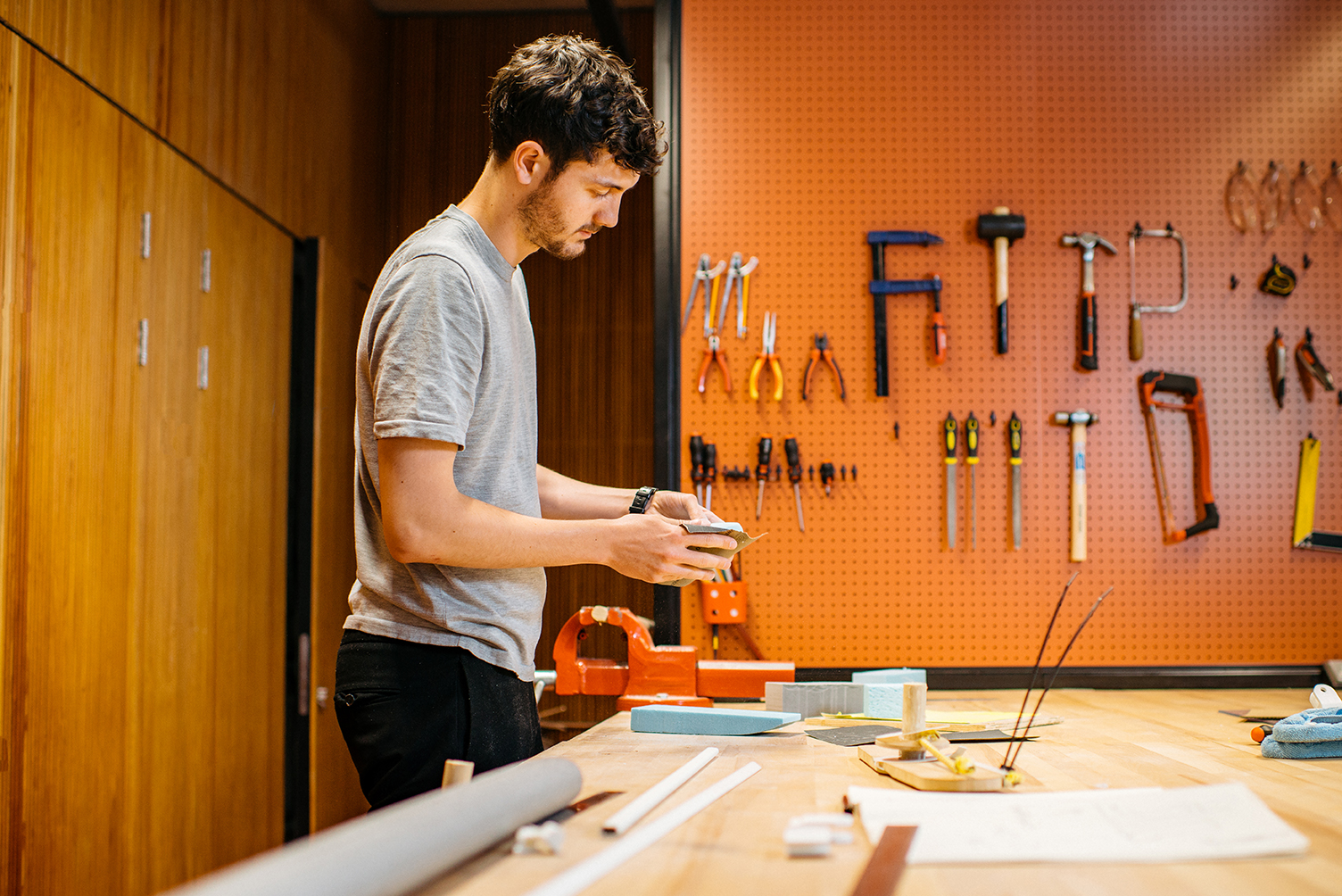 Joseph Joseph workshop with a pegboard tool wall, where a team member shapes a prototype at a large wooden workbench.