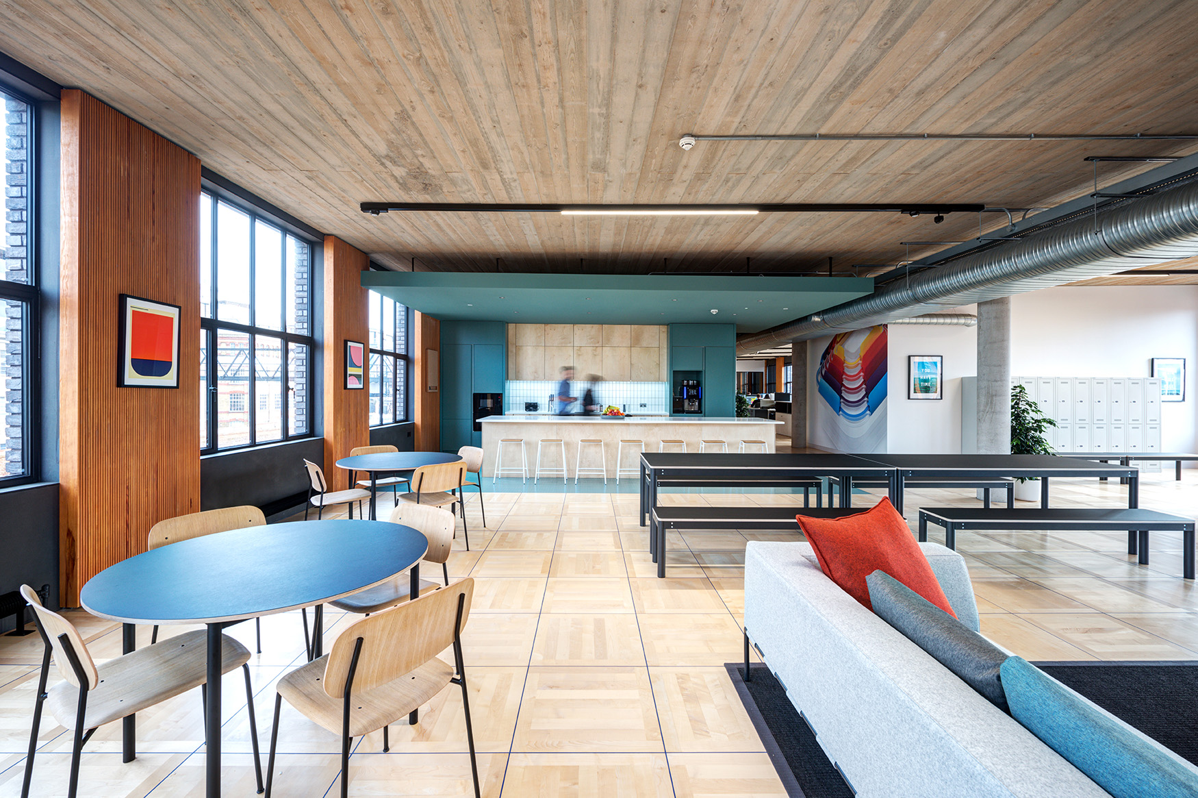 Joseph Joseph office kitchen and breakout space with a central island, dining tables, soft seating, and playful artwork on timber-panelled walls.