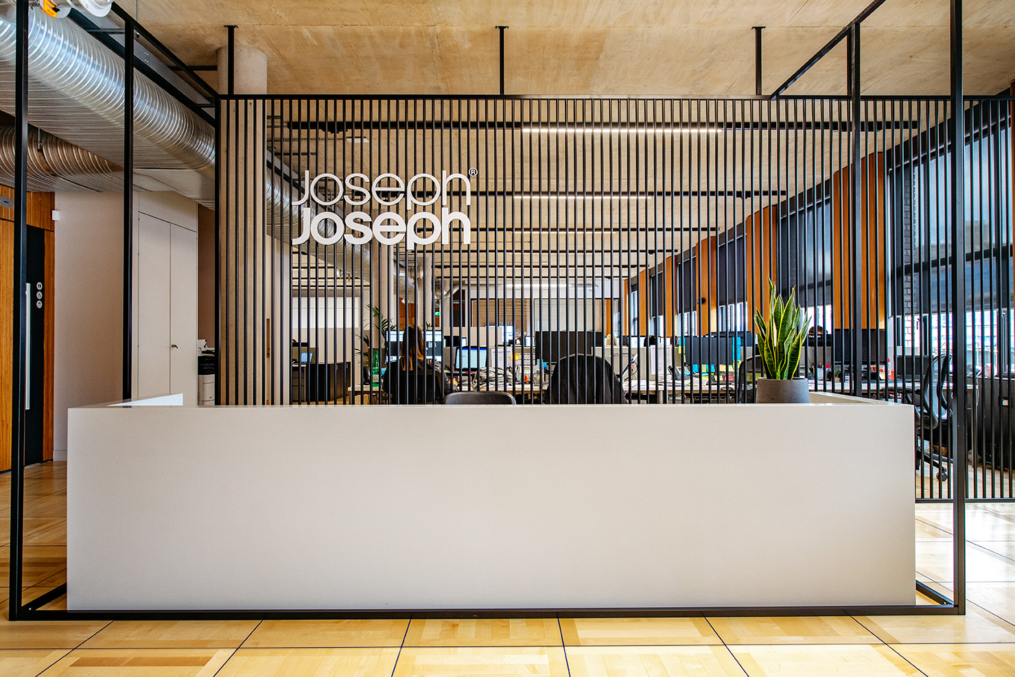 Reception desk at the Joseph Joseph office, framed by vertical timber slats with the company logo and views into the open-plan workspace behind.