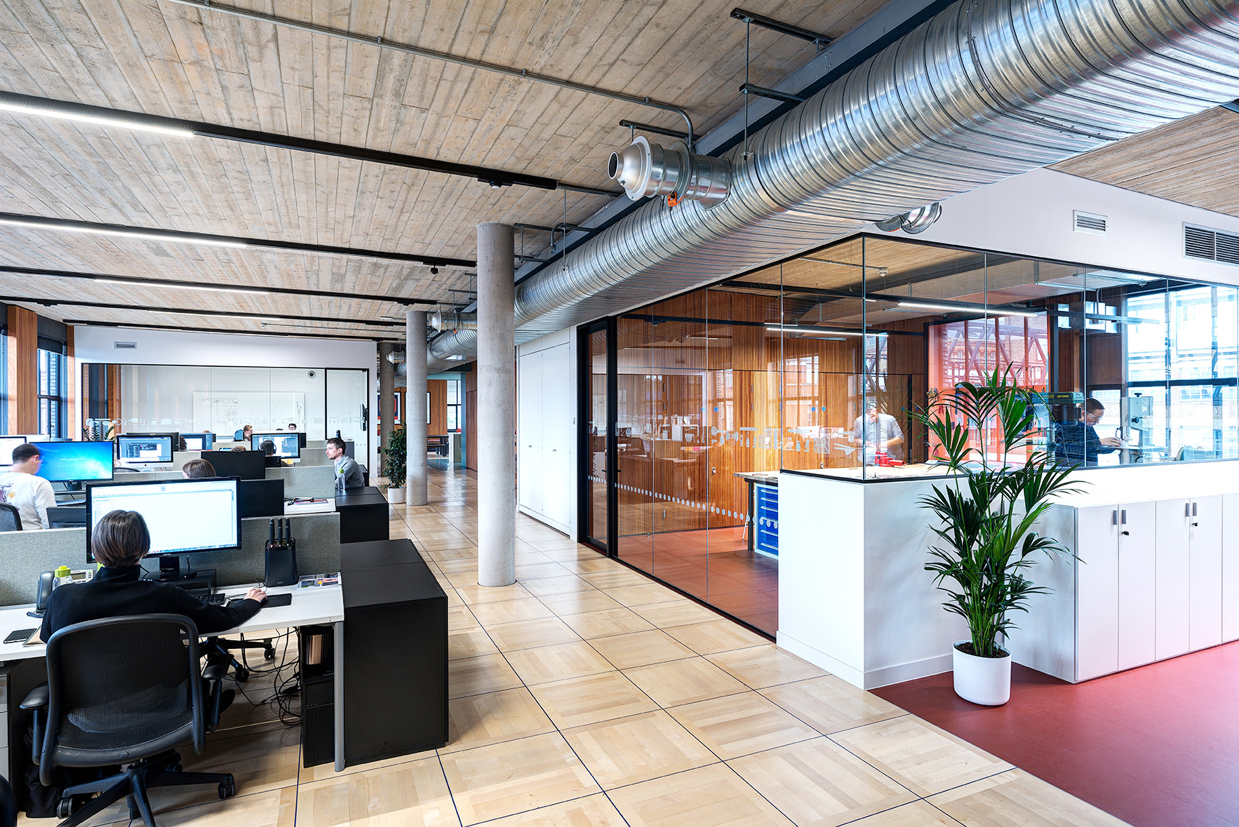 Open-plan workspace at the Joseph Joseph office, with modern workstations, exposed ductwork, and a glazed meeting room with timber panelling.