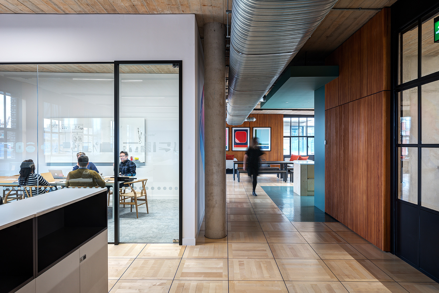 Glass-fronted meeting room and adjacent corridor at the Joseph Joseph office, with exposed services, timber finishes, and a breakout space in view.