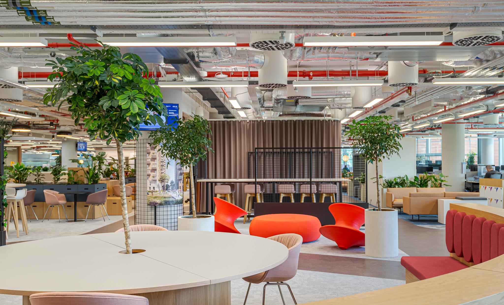 Open-plan breakout area at Landsec’s new HQ, furnished with circular tables, playful red chairs and integrated greenery for a vibrant, collaborative workspace.