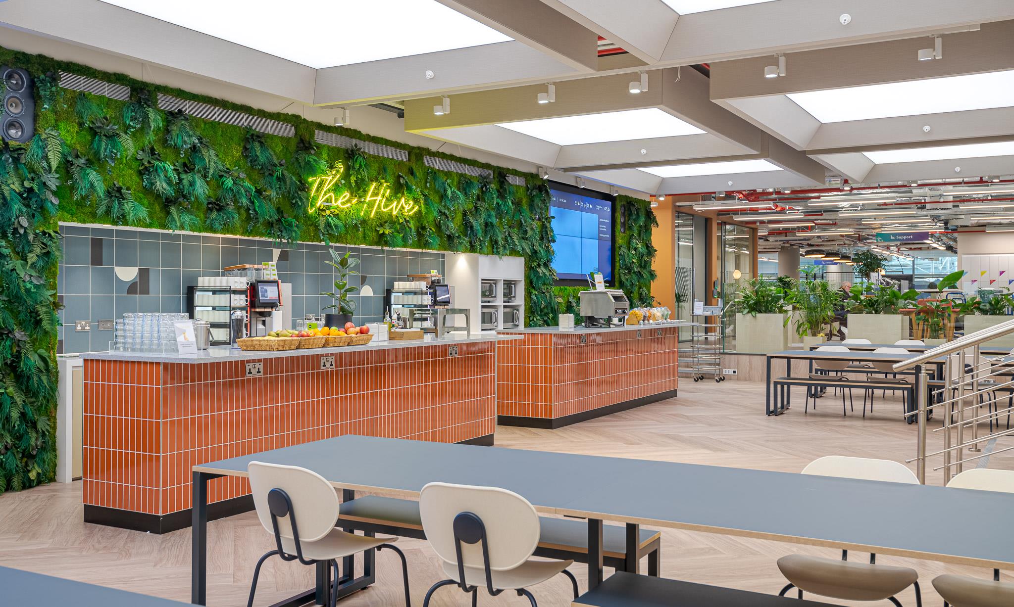 Café-style breakout space at Landsec’s HQ, with tiled counters, biophilic wall design and long communal tables for informal dining and connection.