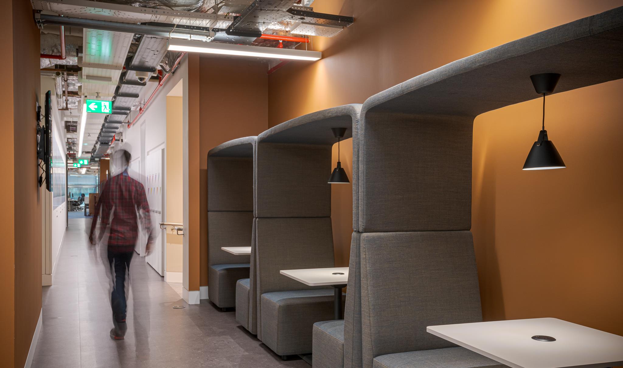 Private work booths at Landsec’s HQ, upholstered in grey fabric with integrated lighting and orange accent walls for focused solo working or quiet meetings.