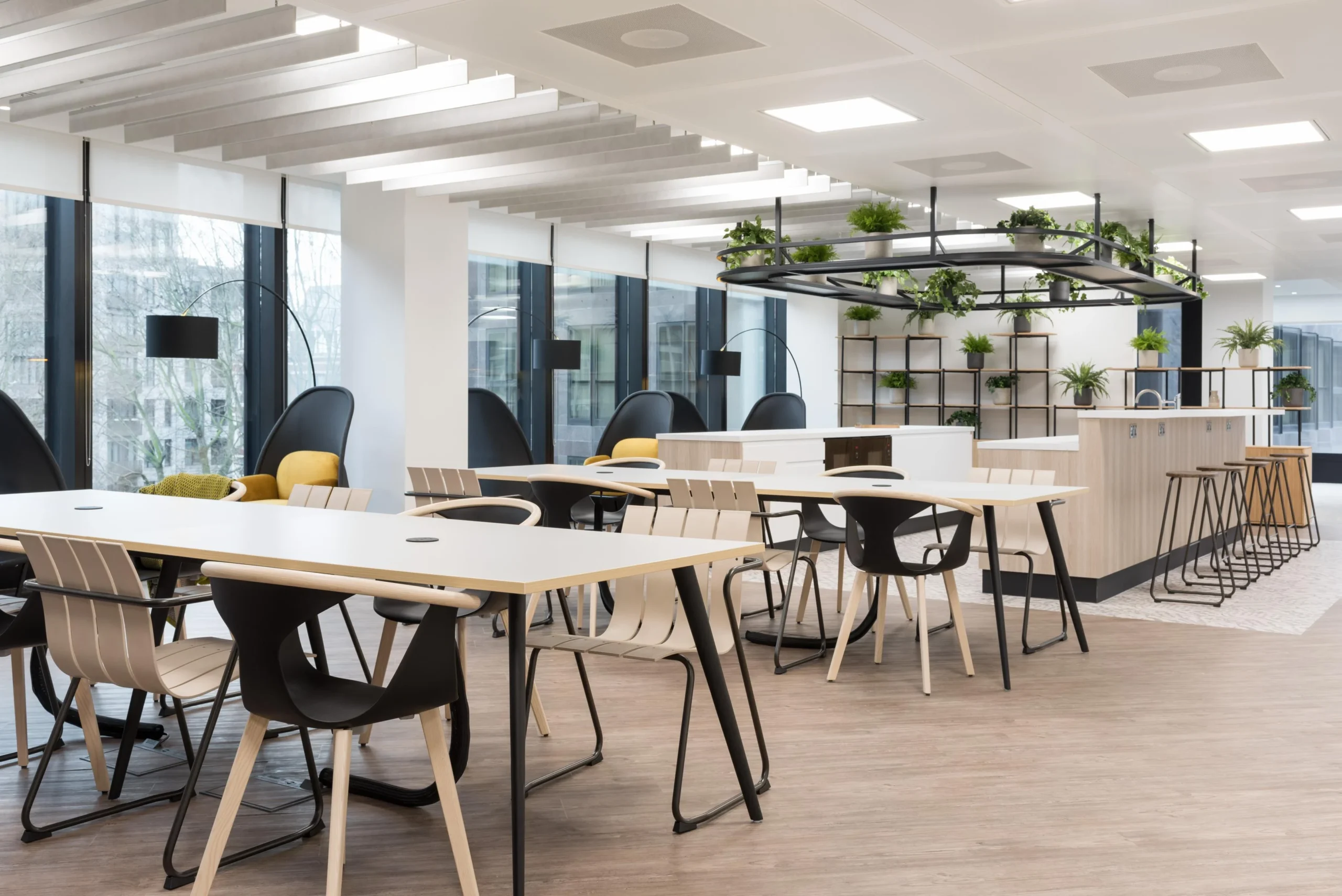Breakout space with furniture supplied for London & Oriental, featuring clean-lined tables, mixed seating, and biophilic shelving under natural light.