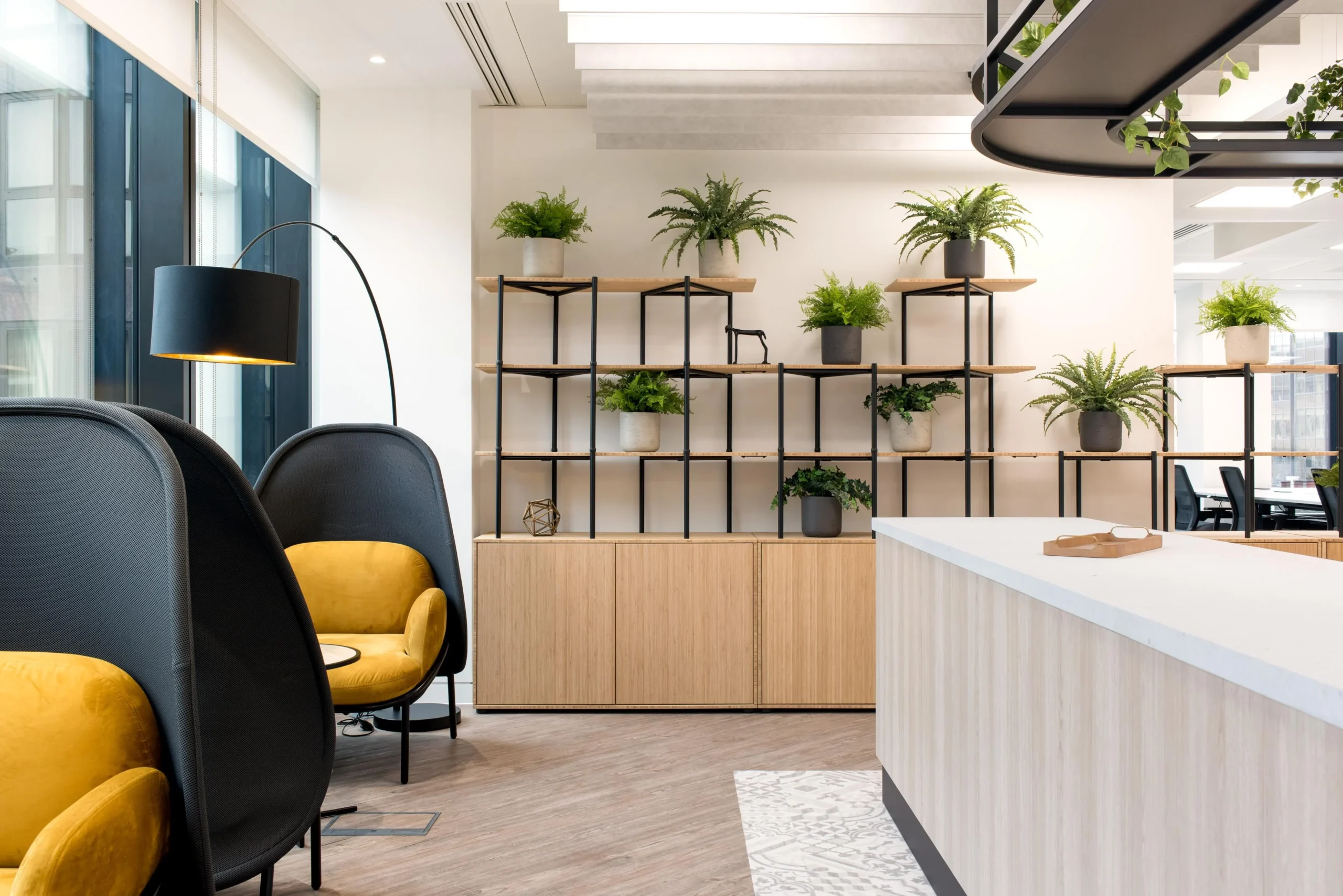 Furniture for London & Oriental featuring high-back lounge chairs in mustard velvet, a black arc floor lamp, and a timber shelving unit styled with plants.