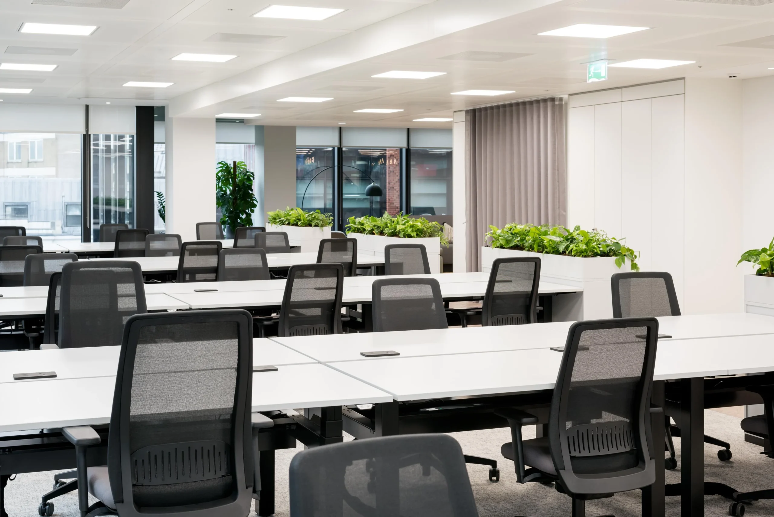 Open-plan workspace for London & Oriental fitted with black mesh task chairs, white bench desks, and integrated planters to define zones and add greenery.
