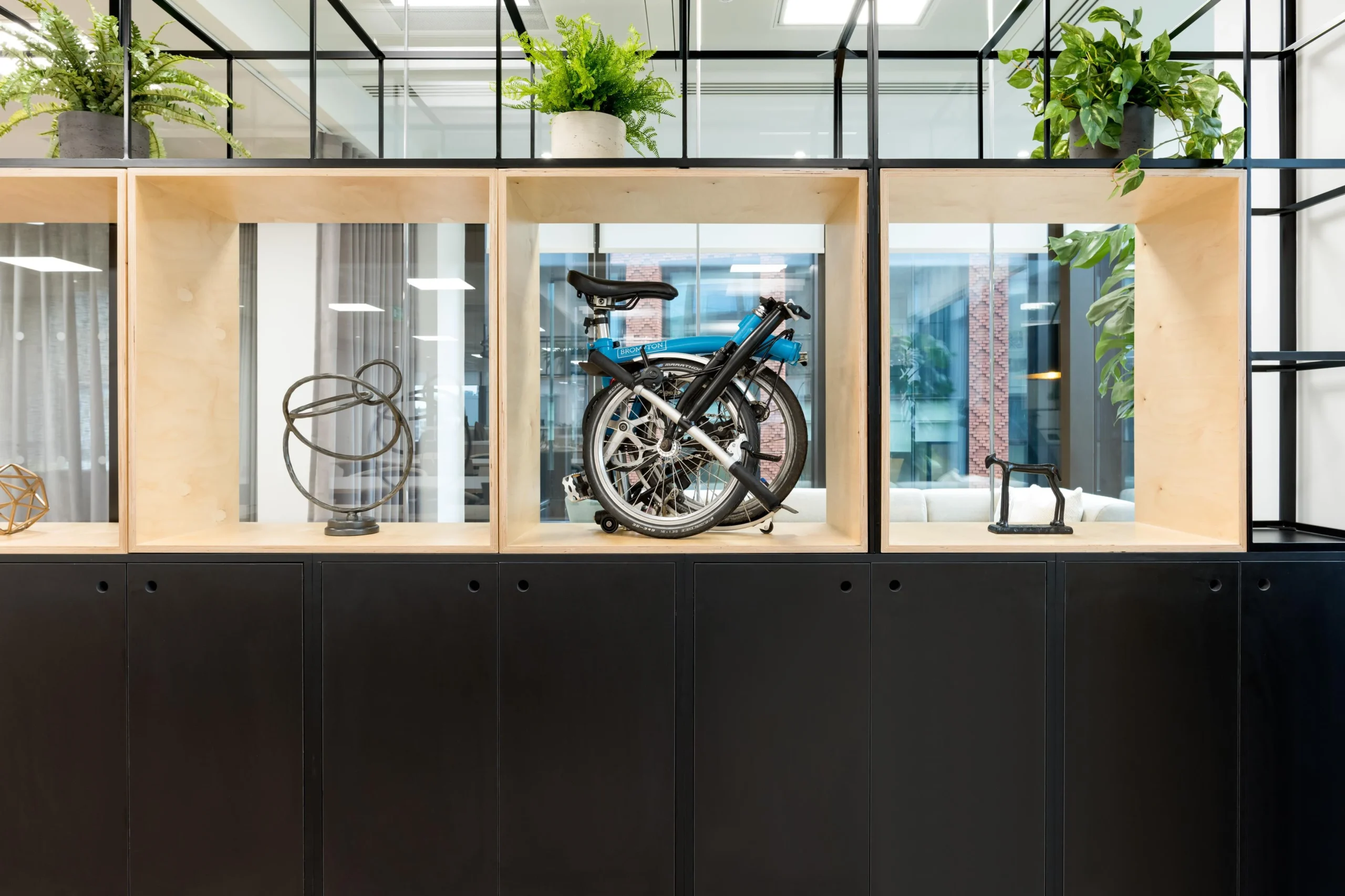 Furniture installation for London & Oriental including bespoke black and timber shelving with integrated storage, styled with plants, ornaments and a Brompton bike.