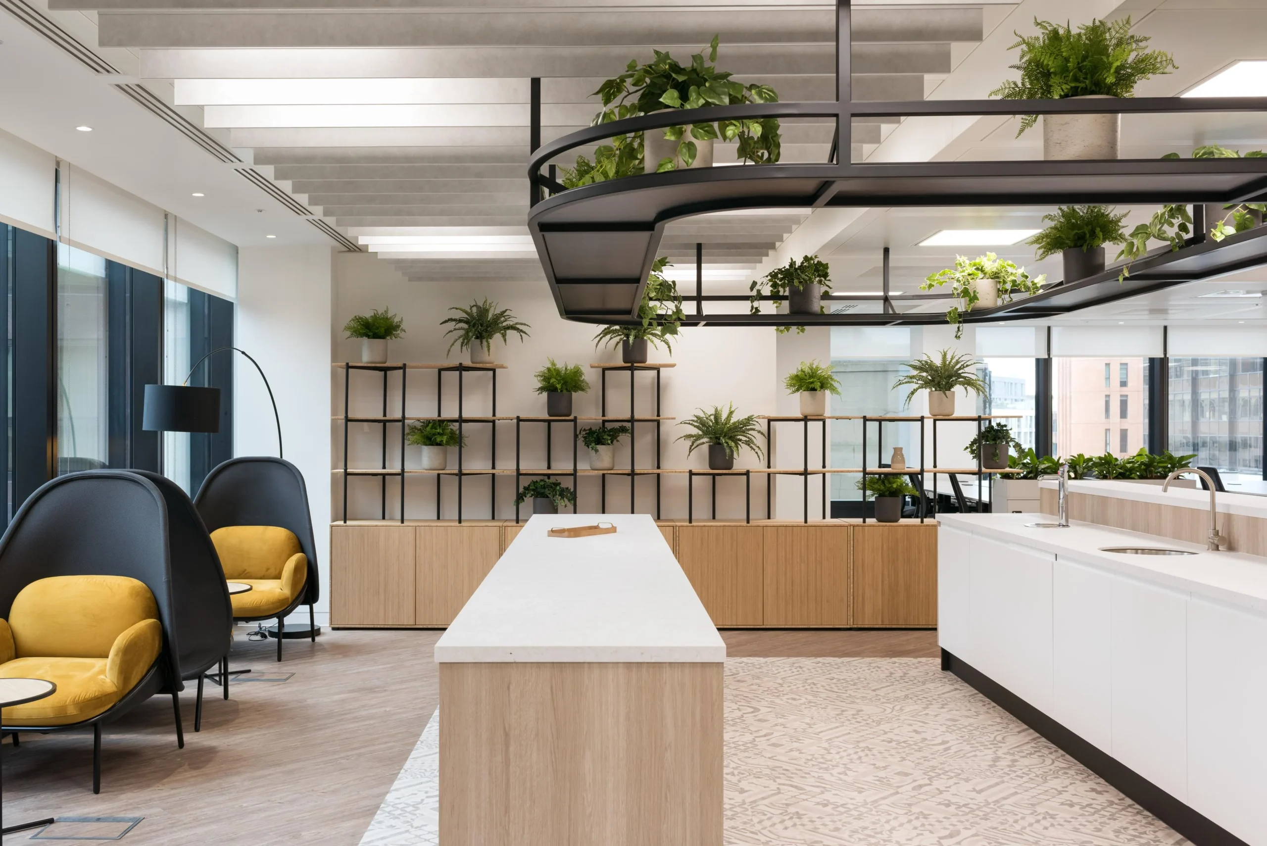 Furniture for London & Oriental’s office kitchen and breakout area, including high-back lounge chairs, timber shelving, and suspended black planters filled with greenery.