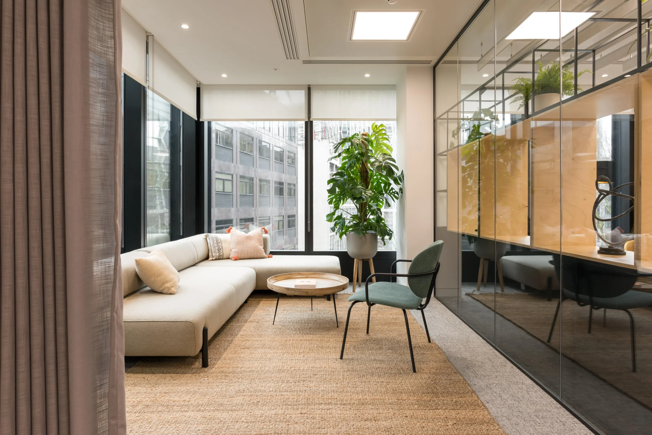 Breakout area furniture for London & Oriental, including a neutral corner sofa, green upholstered armchair and round timber coffee table set against floor-to-ceiling glazing.