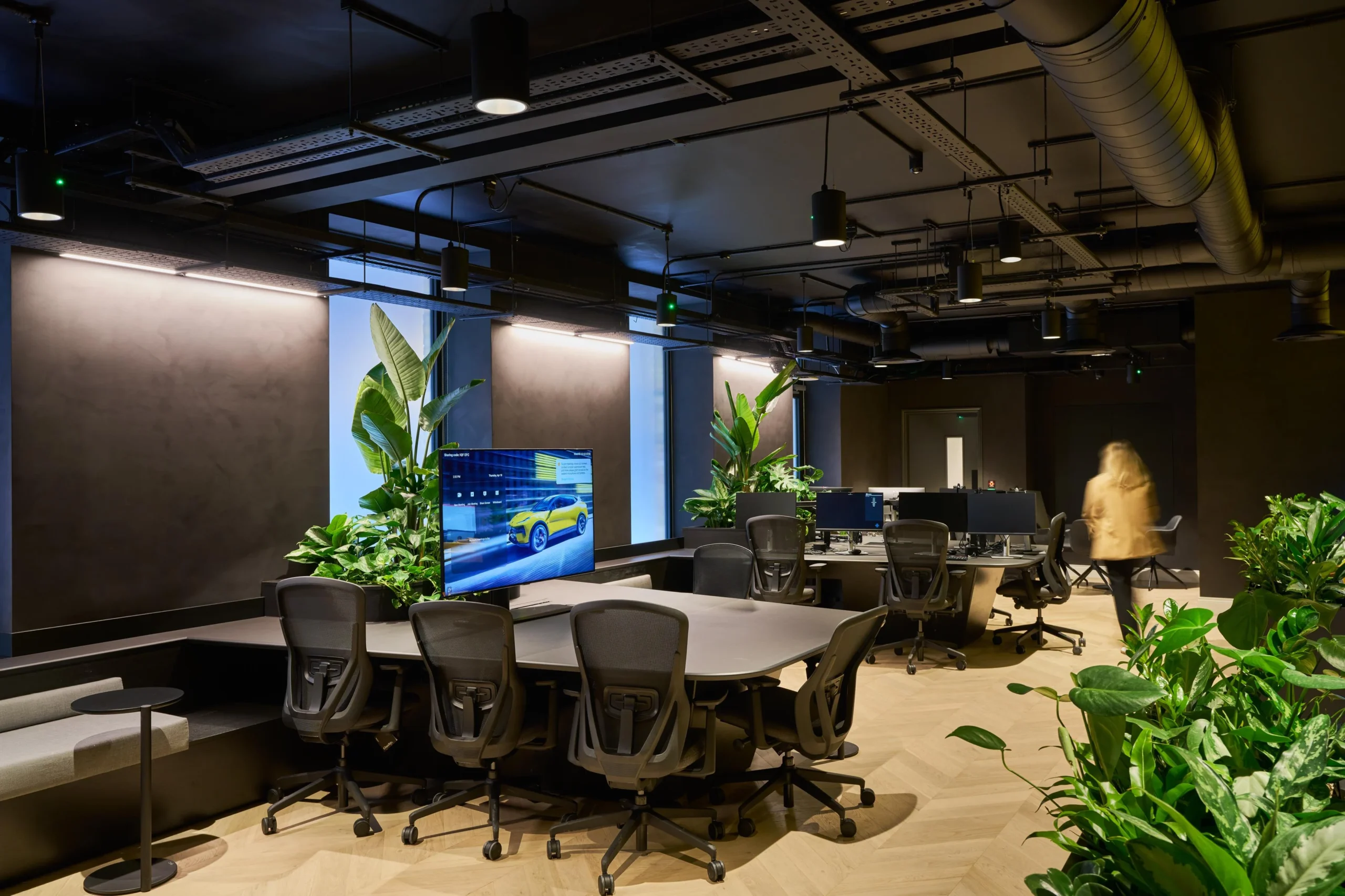 Workstation furniture supplied for Lotus, featuring ergonomic task chairs and collaborative ribbon desking set against a dark, plant-filled office interior.